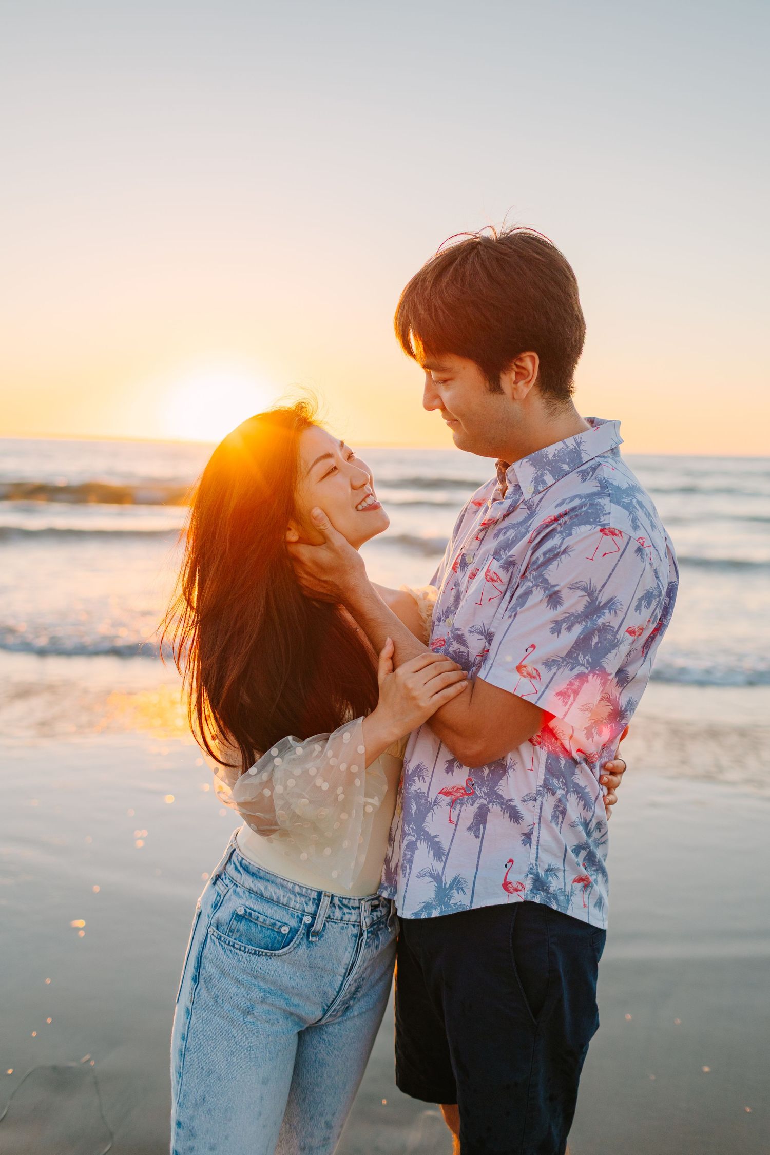 Romantic couple embraces on beach at sunset with golden light illuminating their joyful moment.