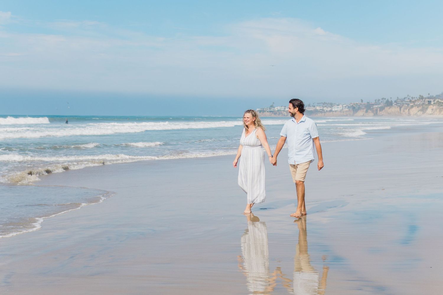Romantic beach photoshoot with gentle waves and cloudy coastal backdrop.
