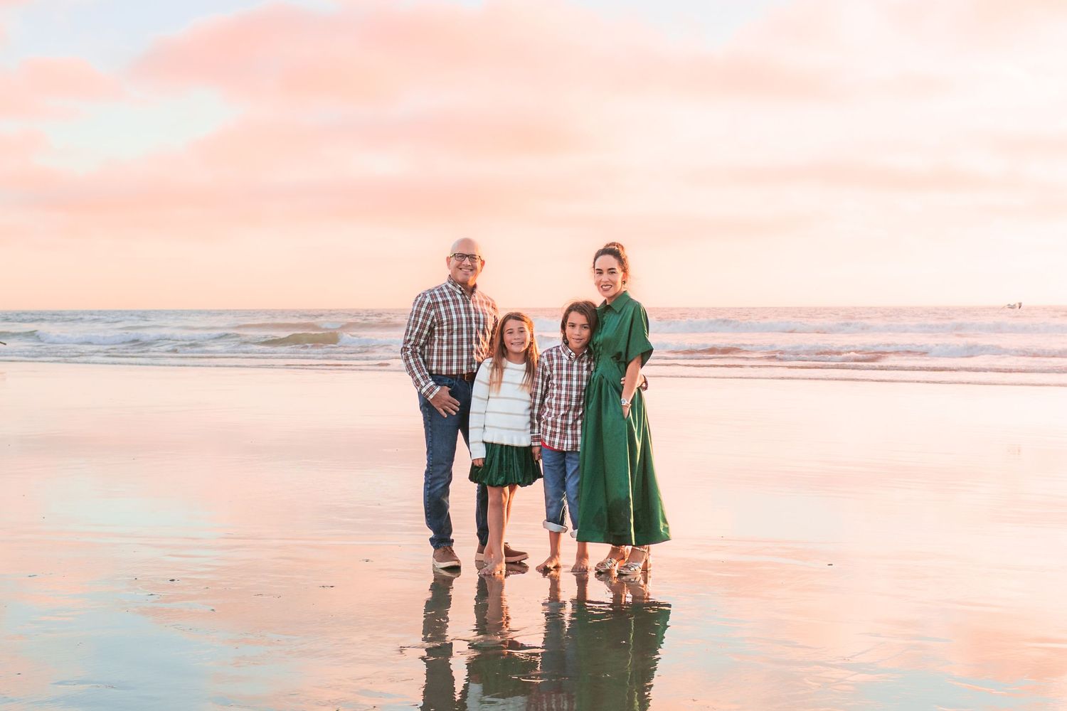 A group enjoying a sunset walk along a serene beach with pink and orange sky reflections on wet sand.