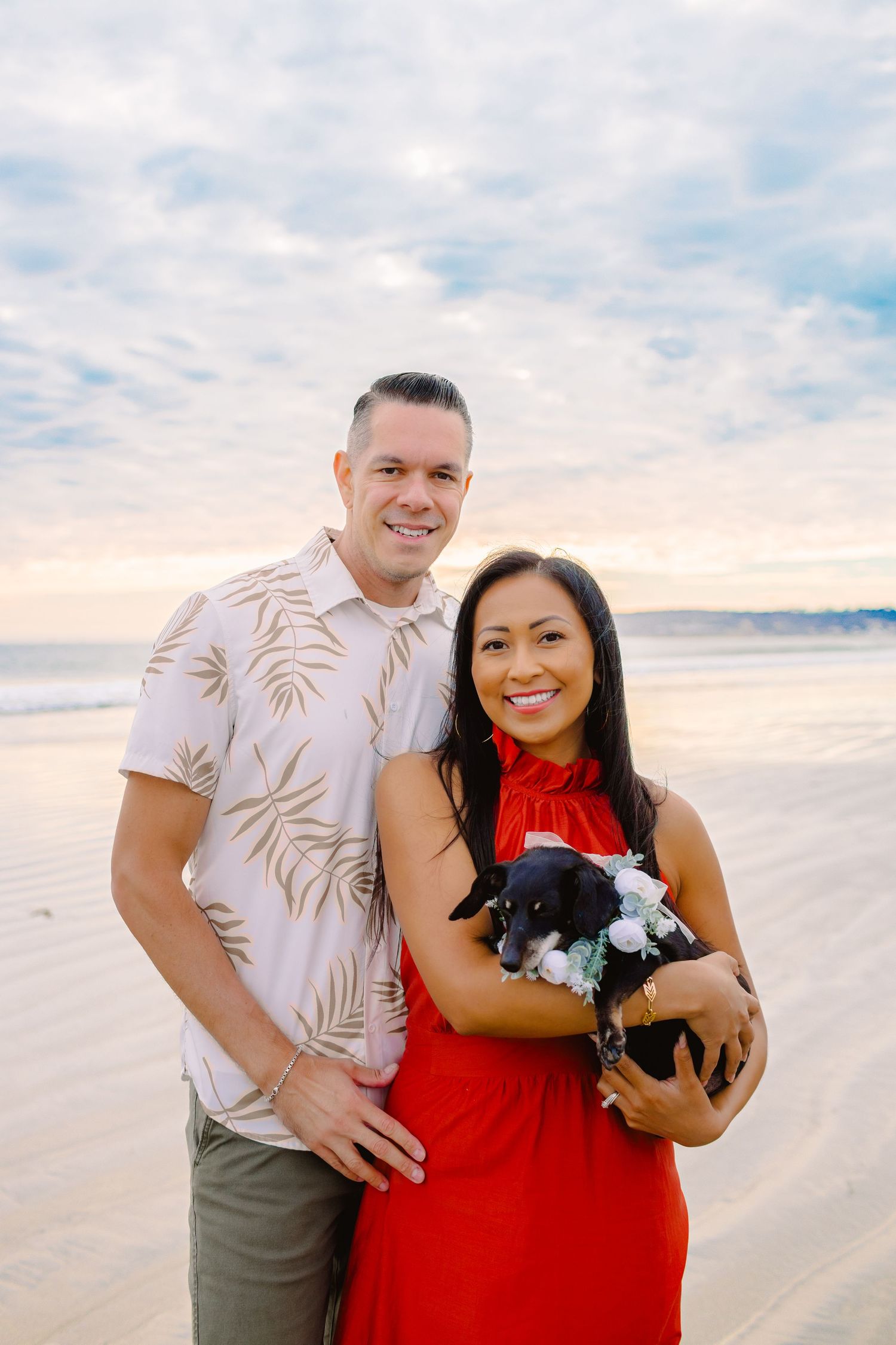 A couple poses together on a beach at sunset with the ocean and pink sky in the background.