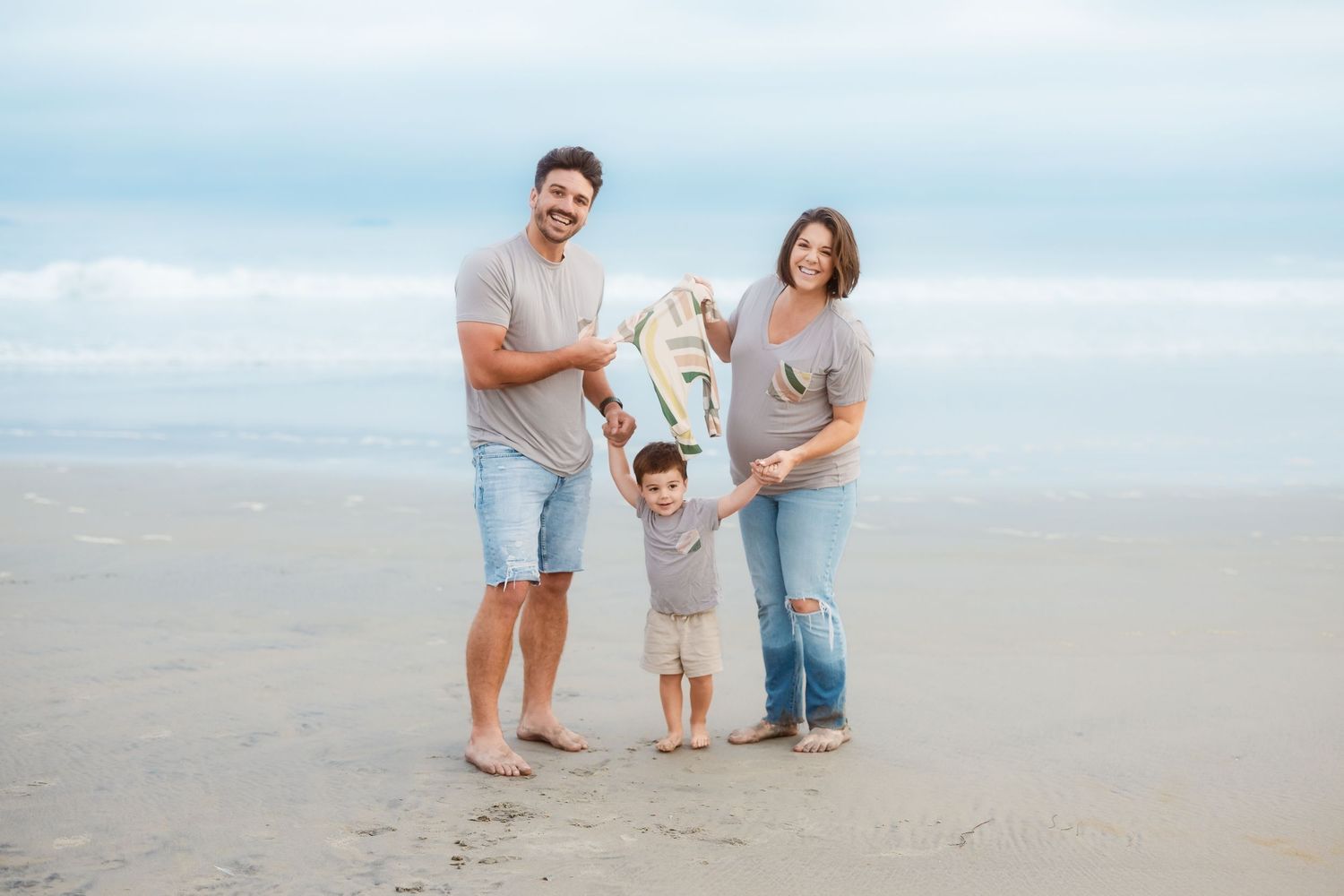A family of three enjoying a tender moment together on a cloudy beach.