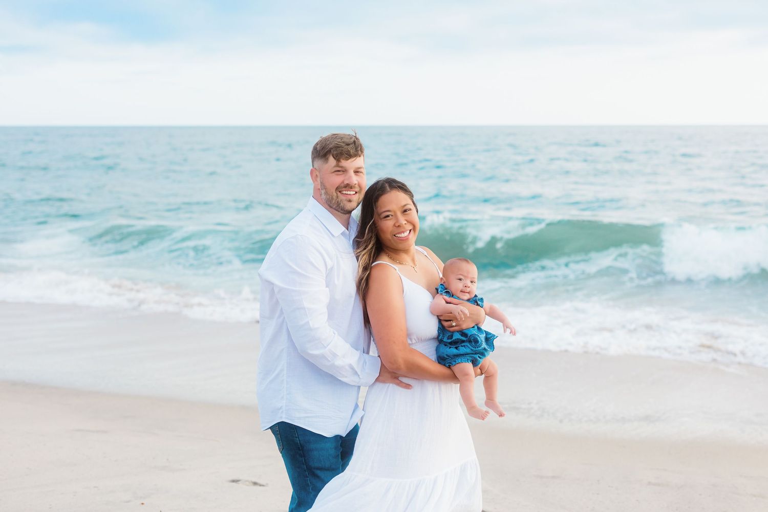 Family enjoying precious moments together on a sandy beach with ocean waves in the background.