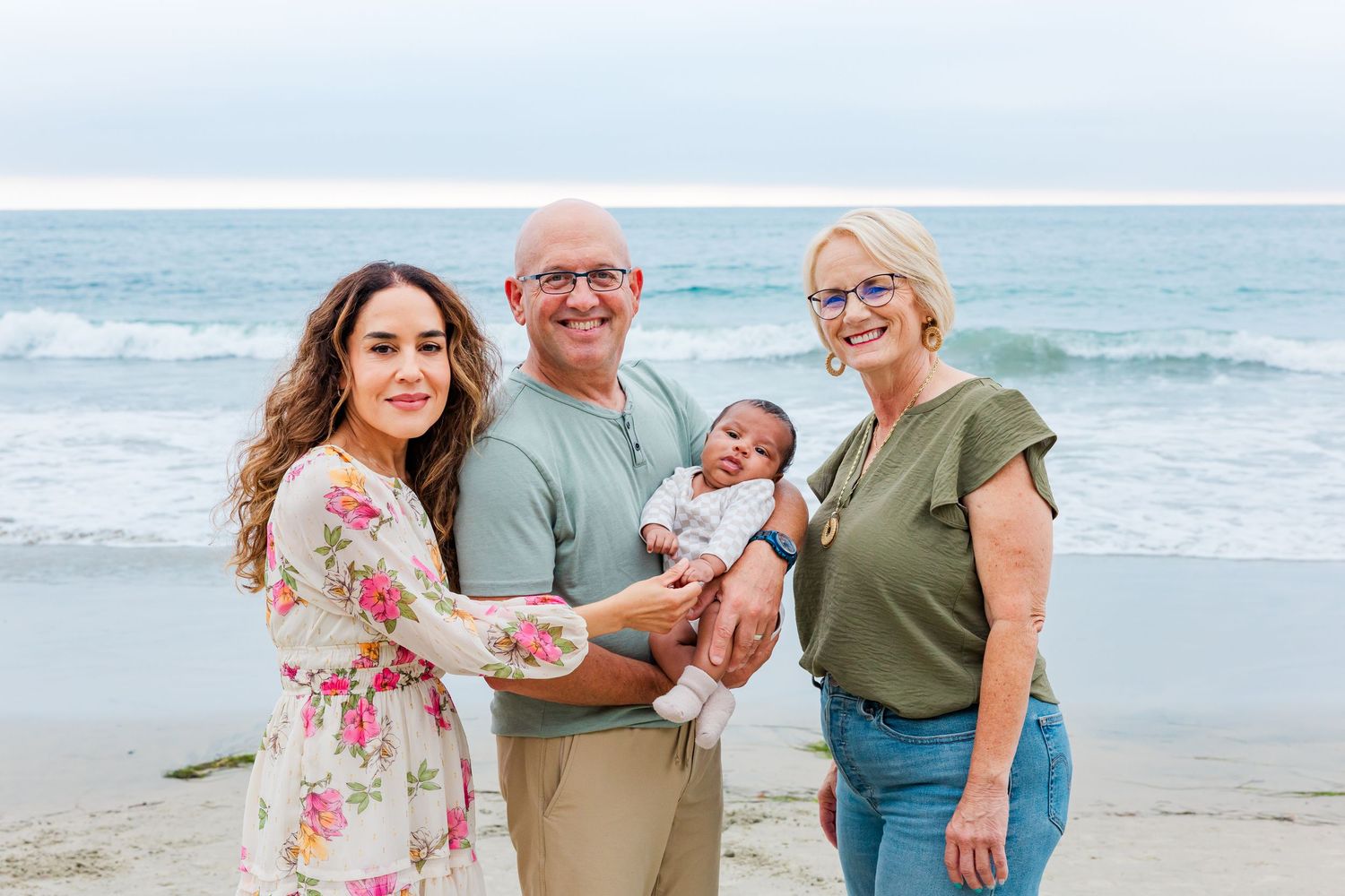 A family portrait on the beach with a small infant against an ocean backdrop.
