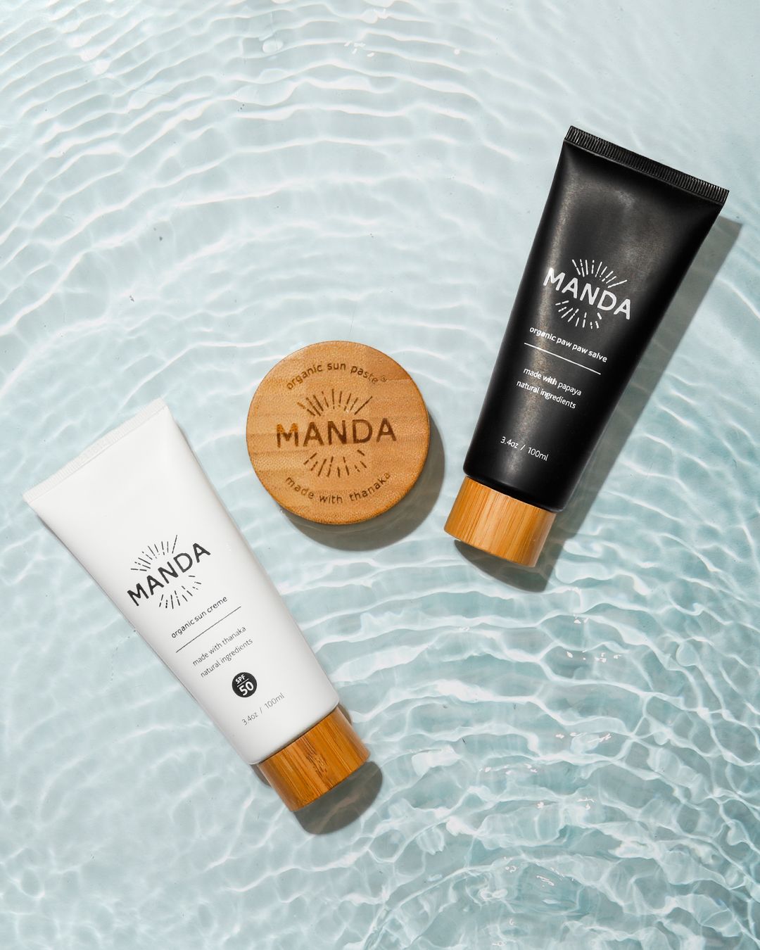 Skincare products from Manda arranged on reflective water surface with ripple effects.