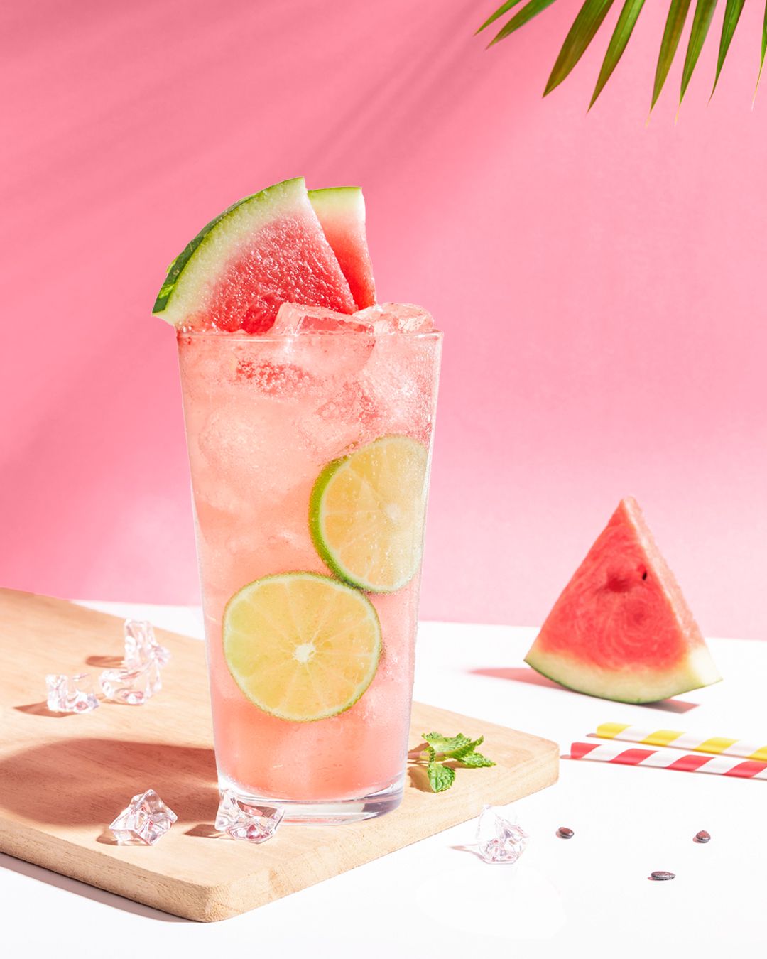 Refreshing watermelon cocktails with lime and ice garnish on pink background.