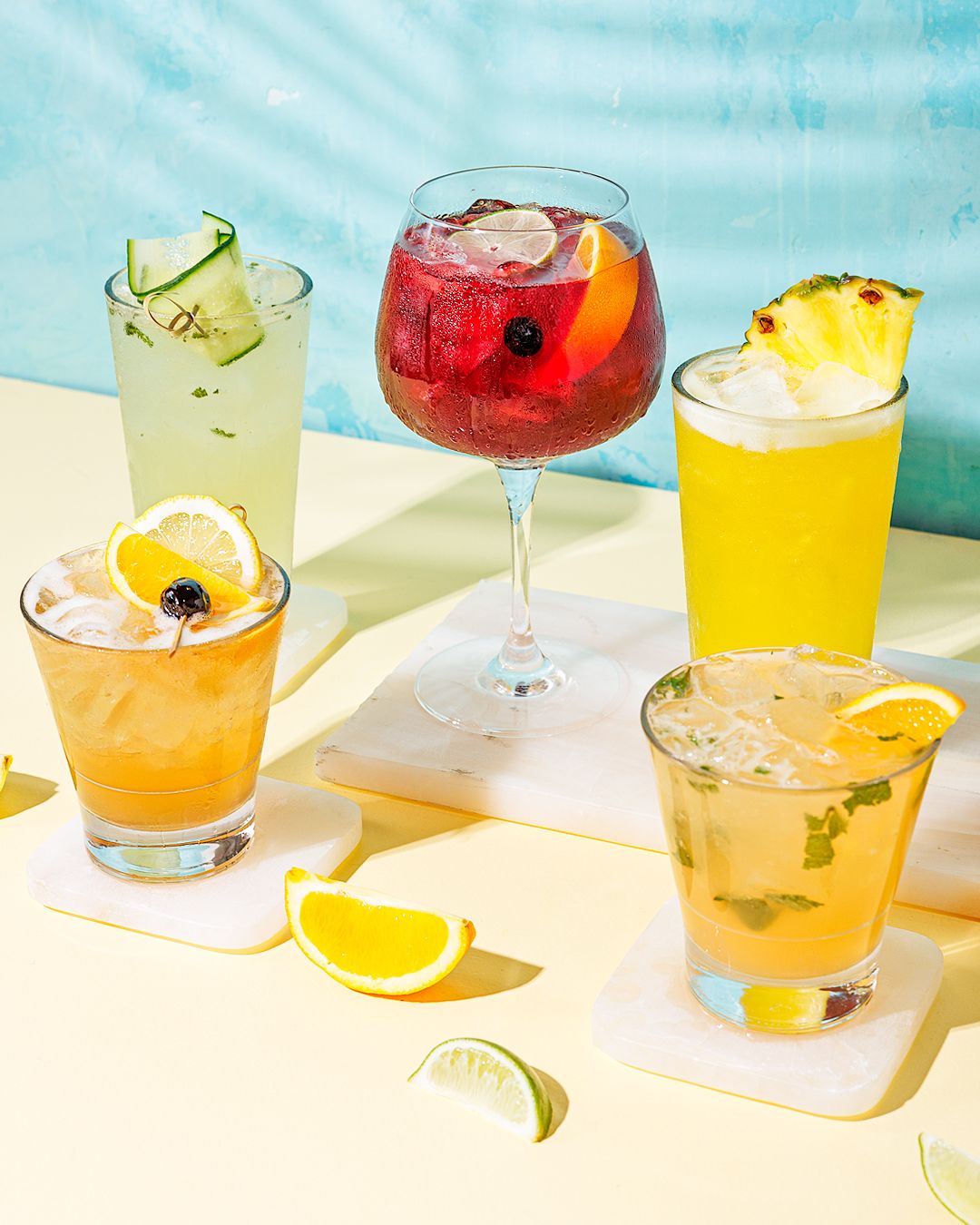 Vibrant summer cocktails in various colors lined up against a turquoise background.