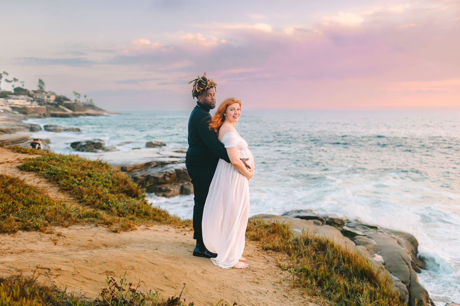 A romantic coastal photoshoot at sunset with crashing waves and rocky cliffs along the California shoreline.