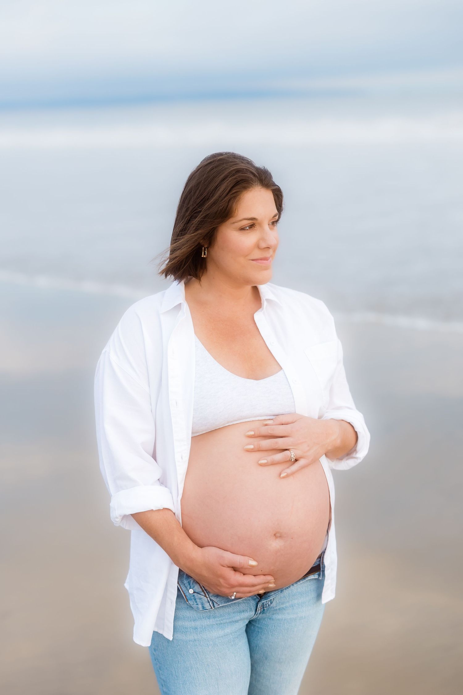Maternity portraits showing an expectant mother in white against a serene beach backdrop.