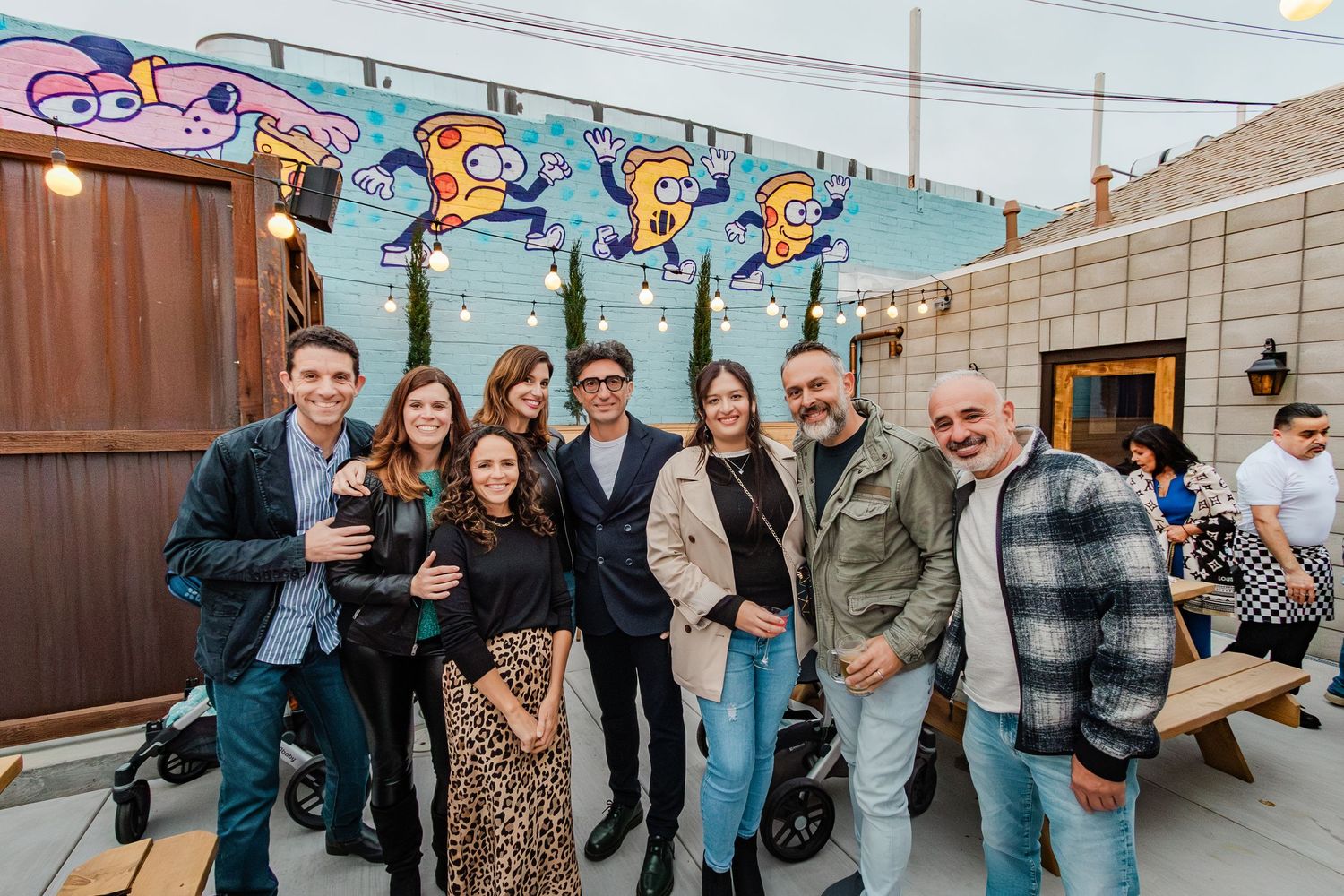Group gathering on rooftop patio with decorative cartoon artwork on wall behind them.