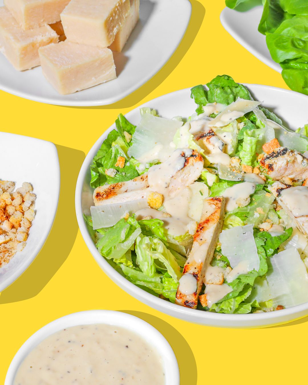 Caesar salad with parmesan cheese and croutons on white plates against yellow background.