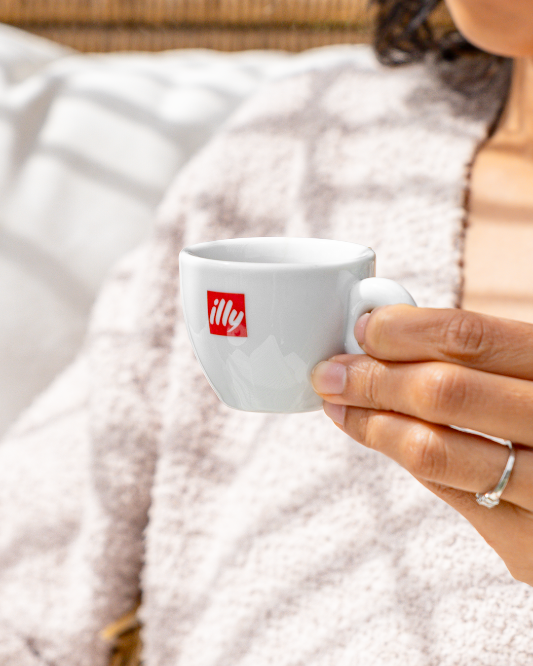 Hand holding small white illy espresso cup against textured white background.