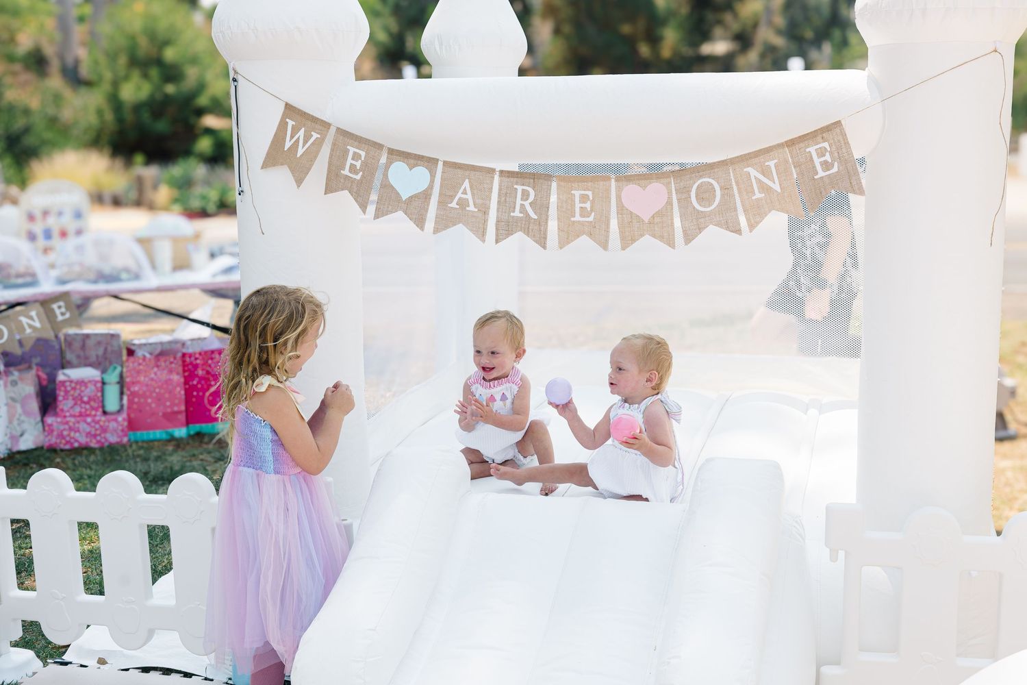 White picket fence party setup with pastel decorations and banners in a park.