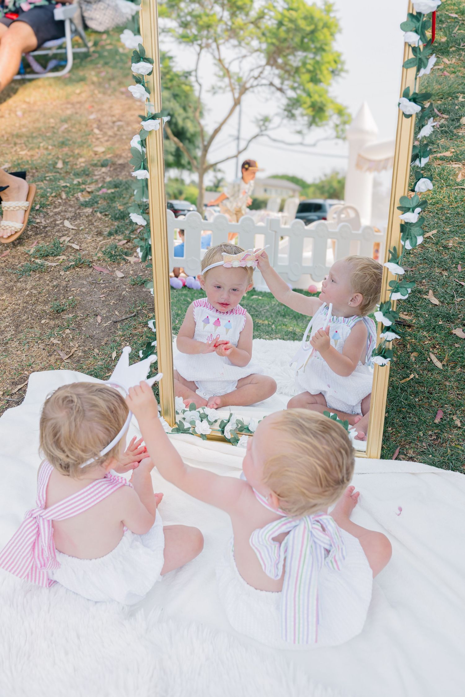 Adorable babies having fun outdoors reflected in mirror frame during festive party setup.