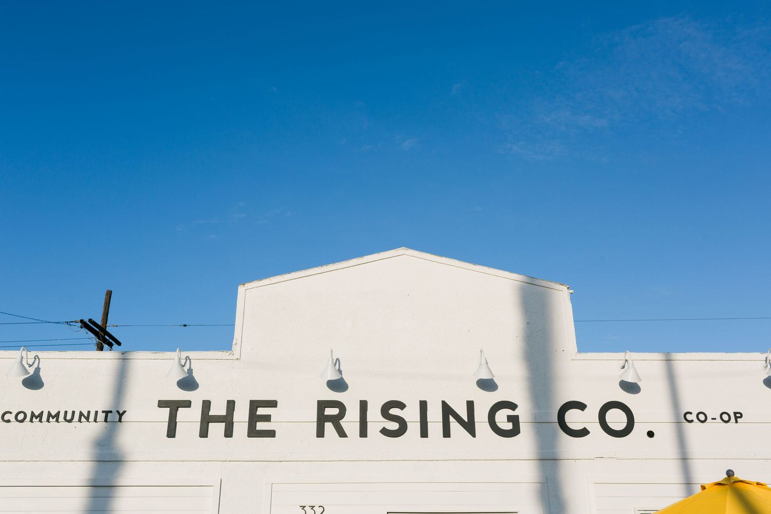 Panoramic view of The Rising Co building facade against a bright blue sky with white industrial architecture.