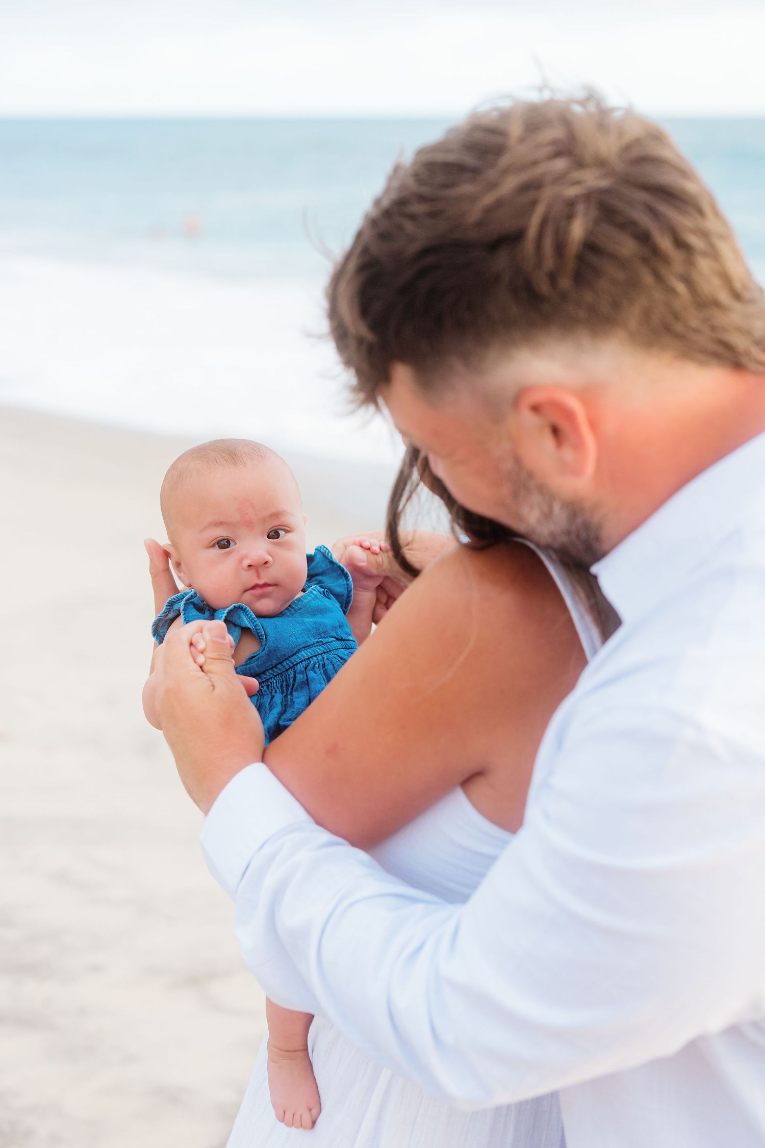 An intimate family moment with a baby in blue on a sunny beach.