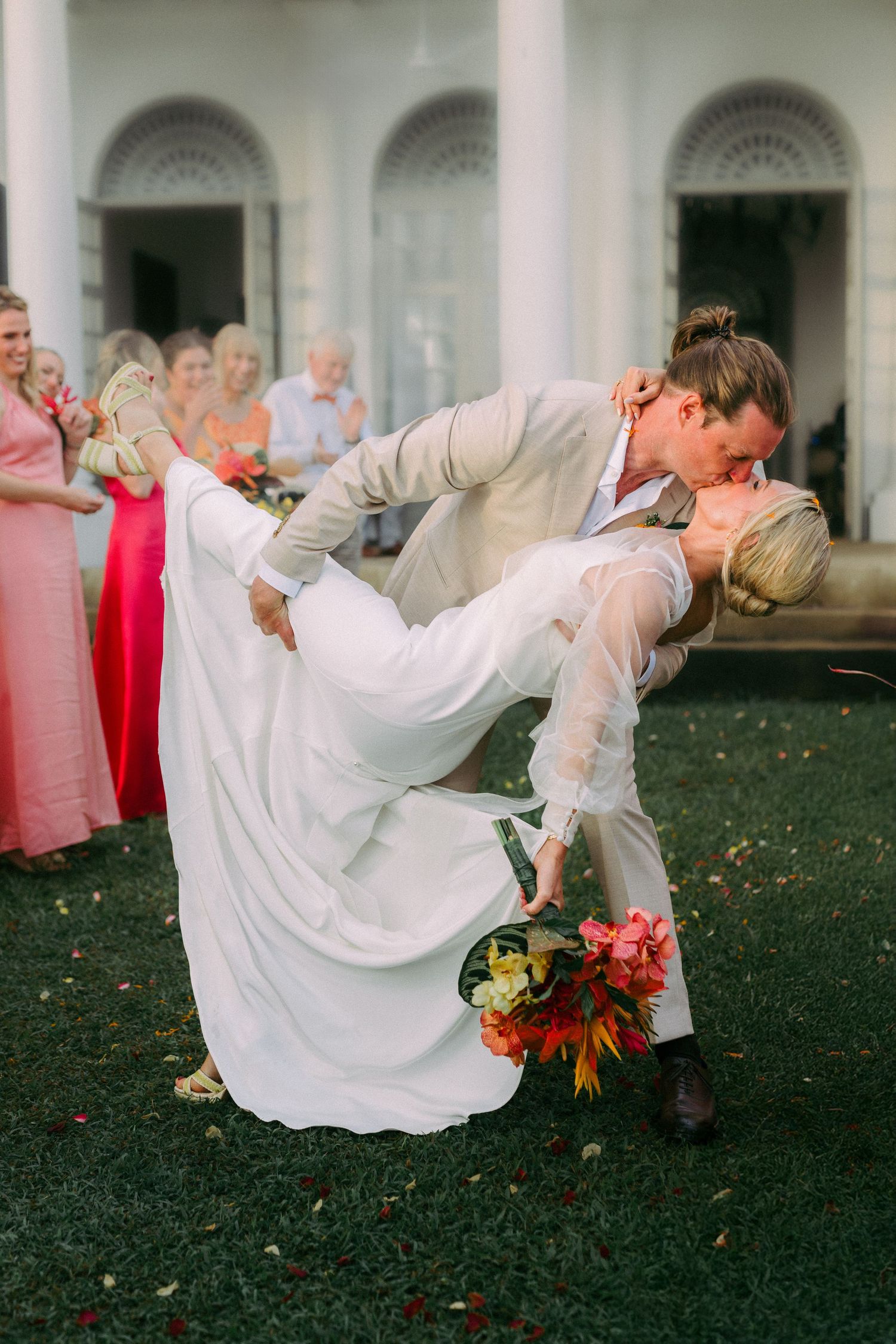 Romantic wedding dip kiss with couple surrounded by guests in formal attire.