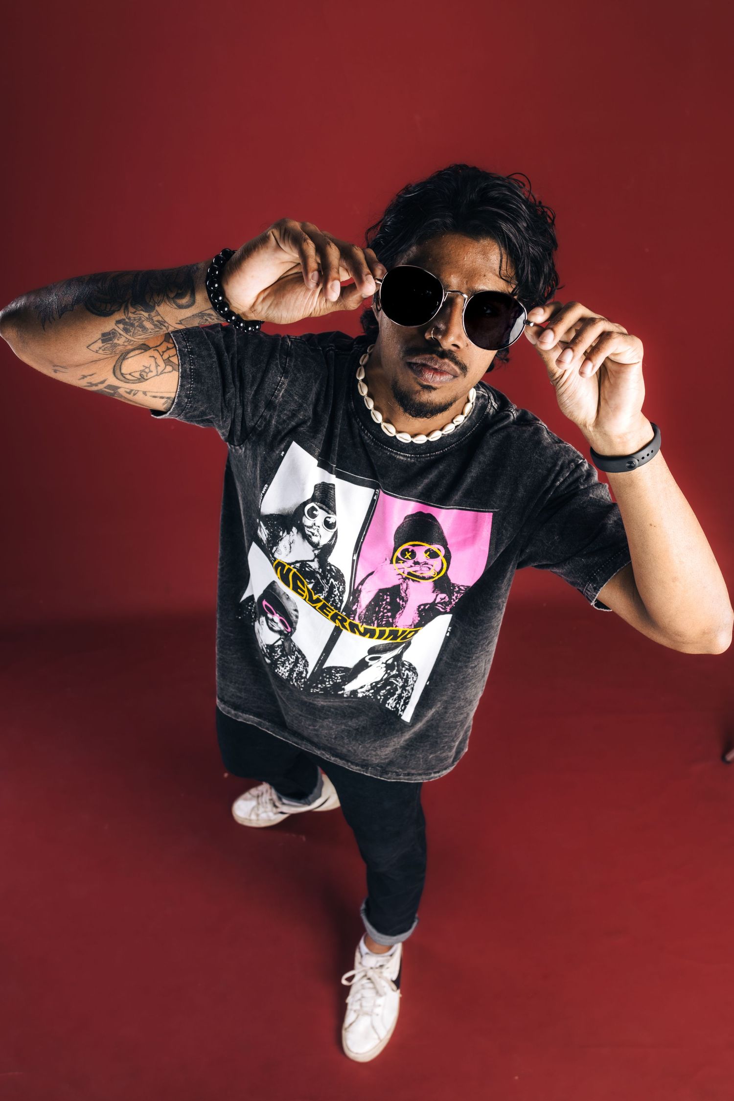 Person in graphic band t-shirt posing with sunglasses against red background.