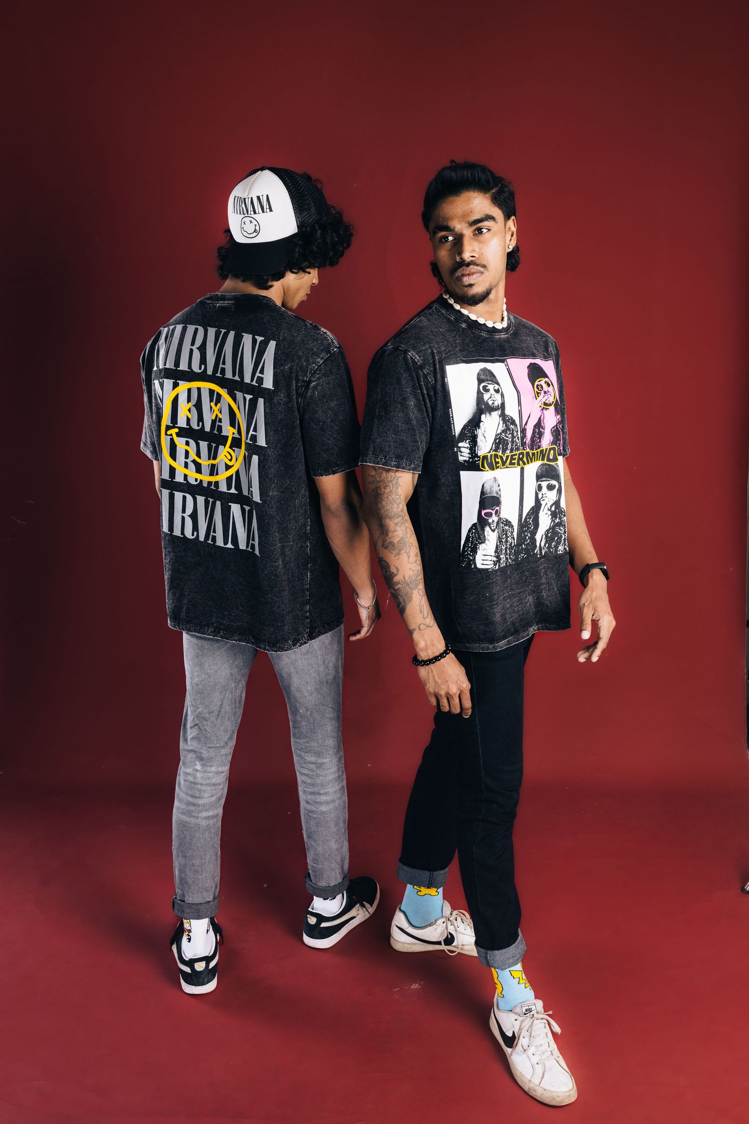 Two people wearing vintage Nirvana t-shirts pose against red background.