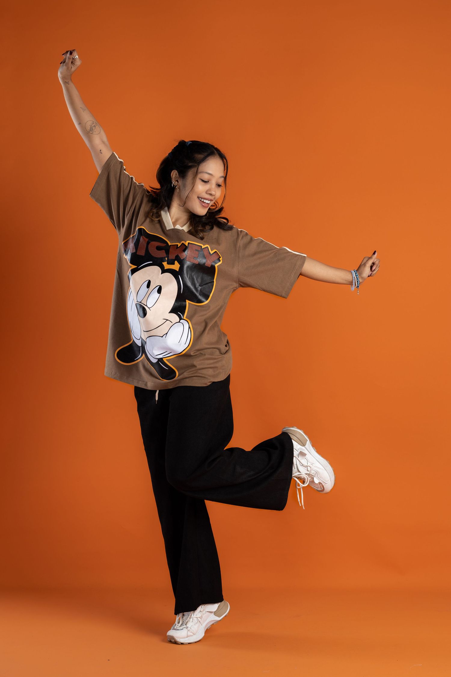 Person in Mickey Mouse t-shirt strikes dynamic dance pose against orange background.