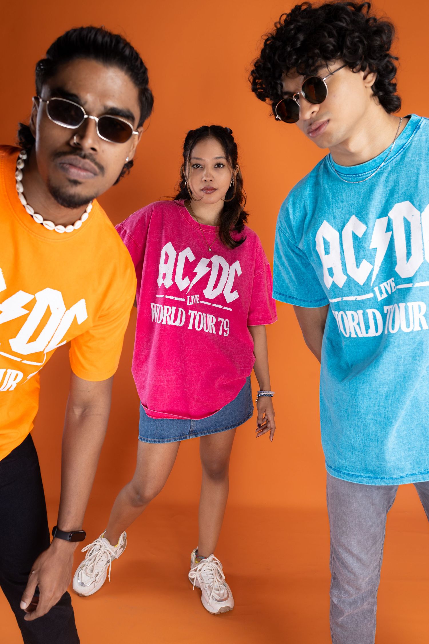 Three people wearing colorful AC/DC World Tour t-shirts pose against orange background.