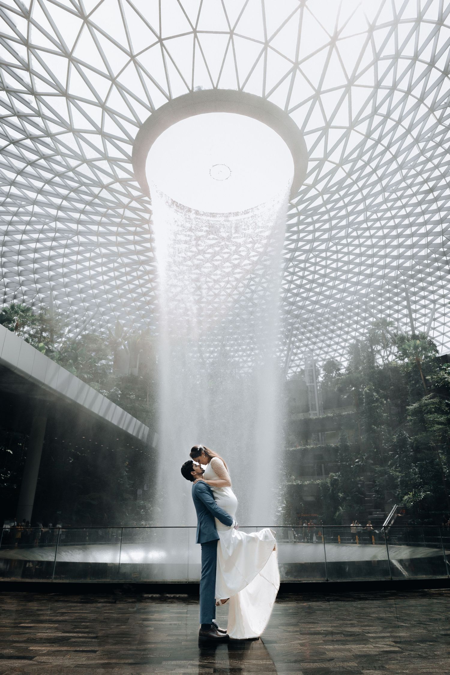 Romantic couple embracing under architectural dome with dramatic water feature.