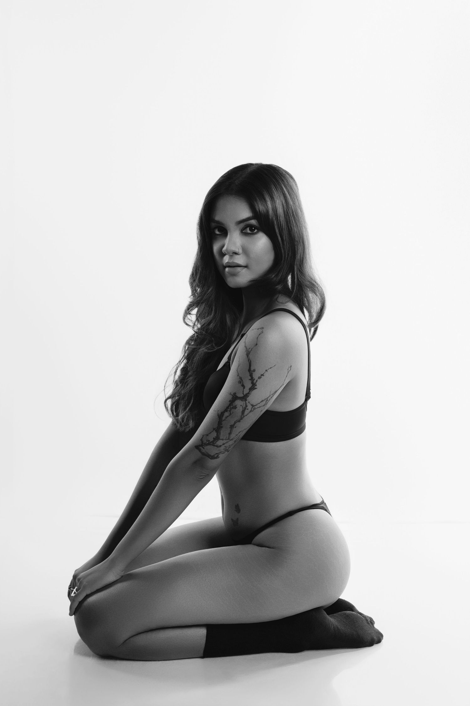 A black and white artistic studio portrait of a person posing in athletic wear on a white background.