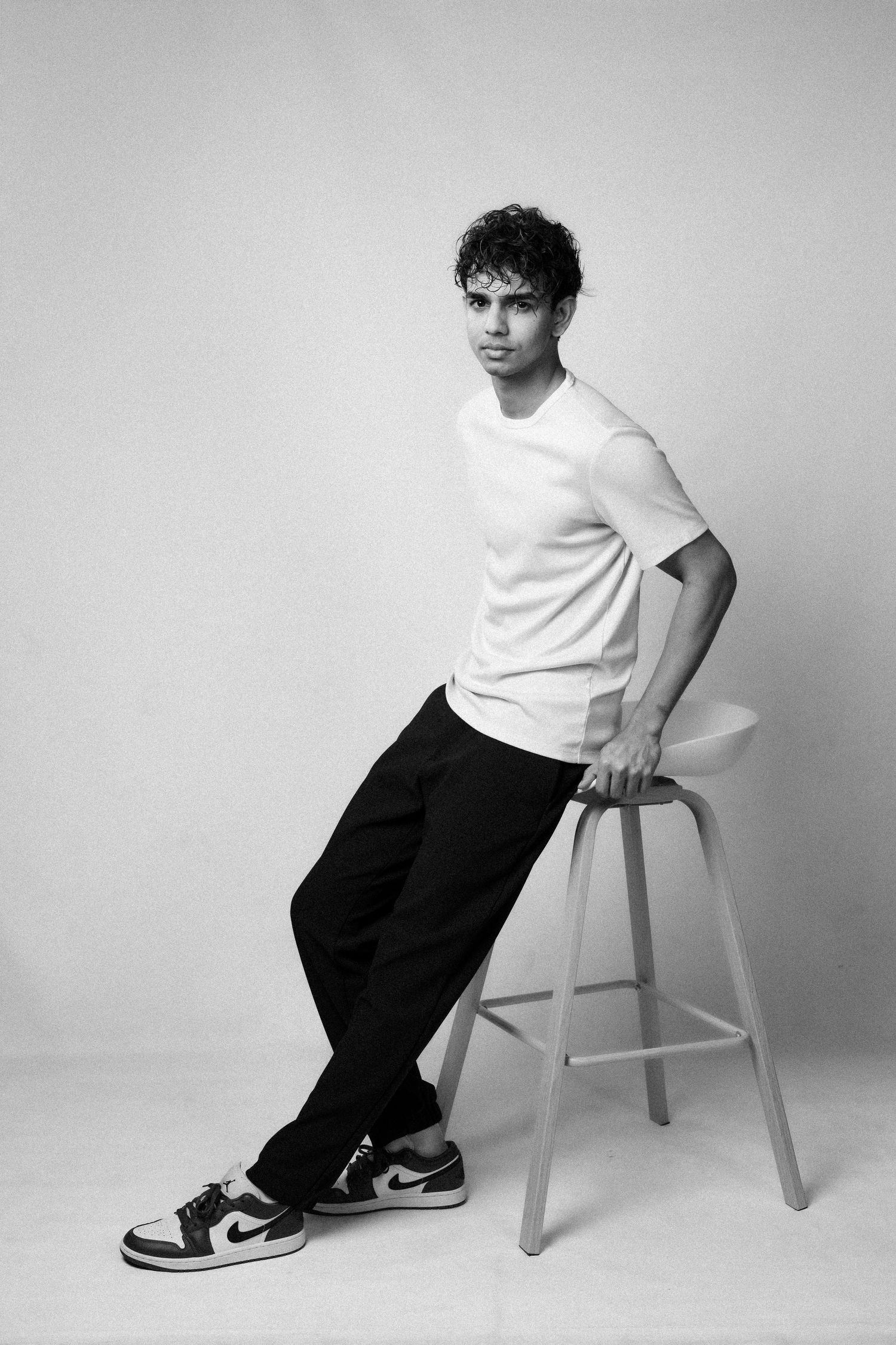 Black and white studio photo with someone posing on a stool.