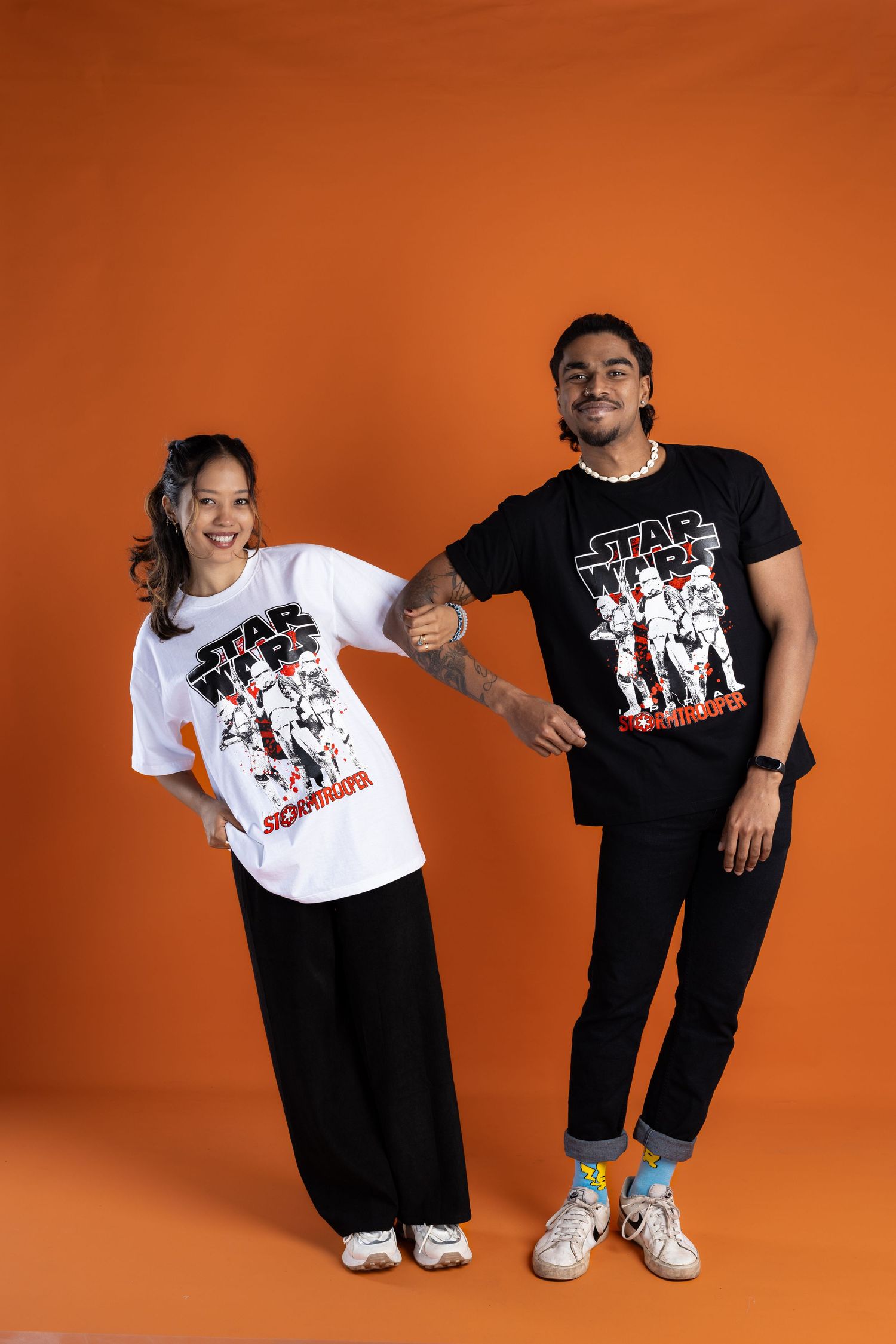Two people wearing matching Star Wars graphic t-shirts pose against an orange background.