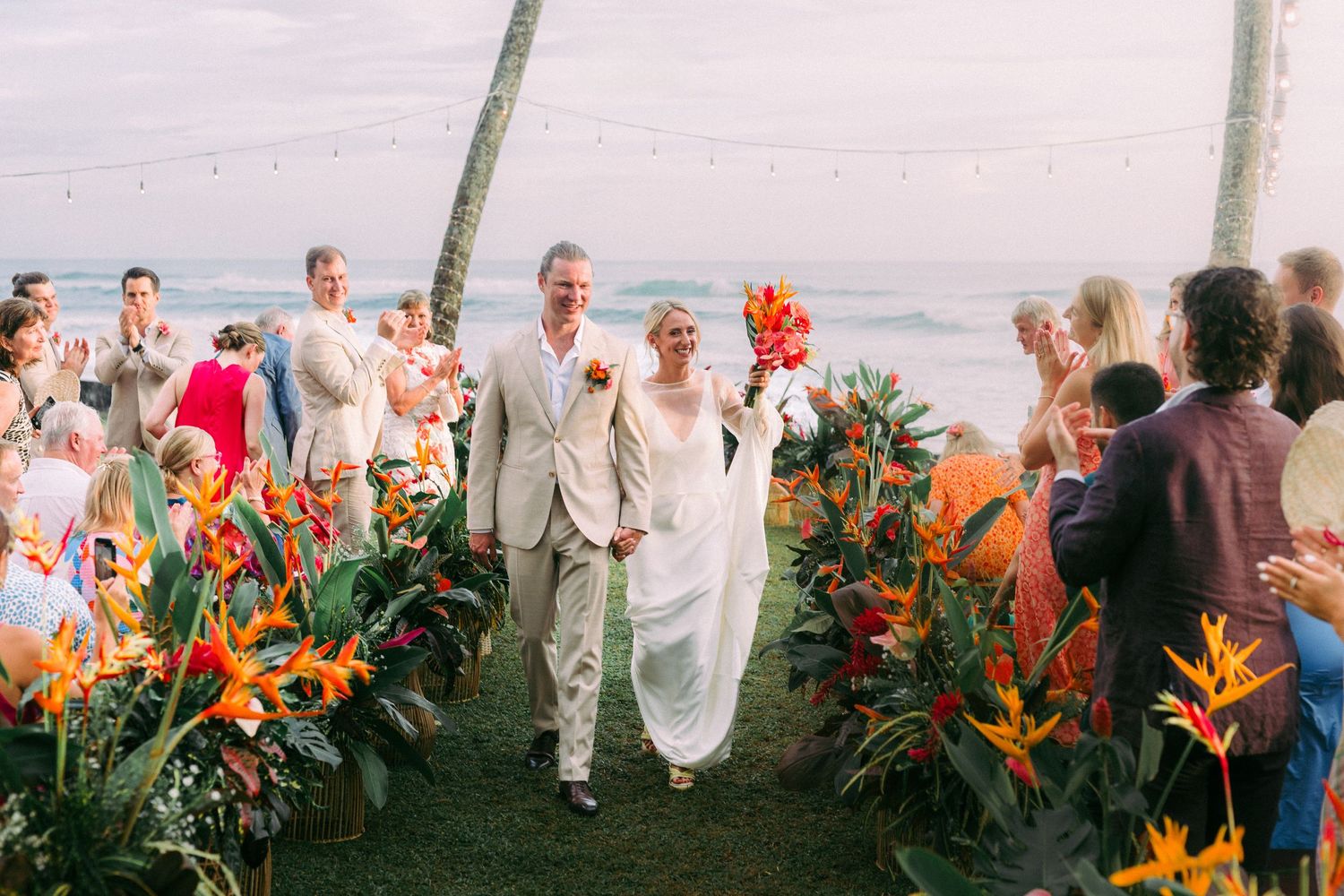 Wedding ceremony with couple walking through vibrant orange bird of paradise flowers.