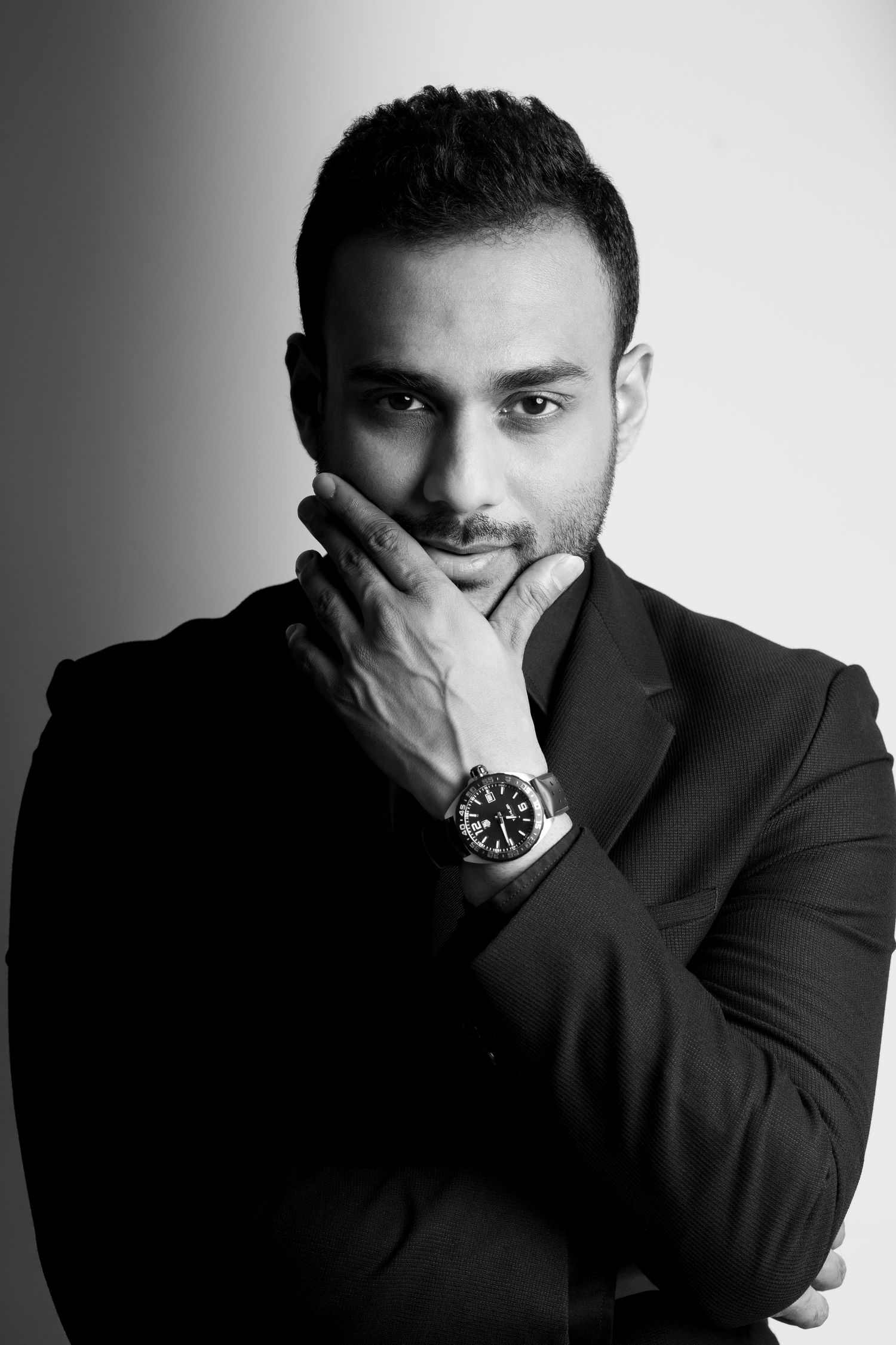 Professional headshot of man in dark suit with hand thoughtfully placed on chin.