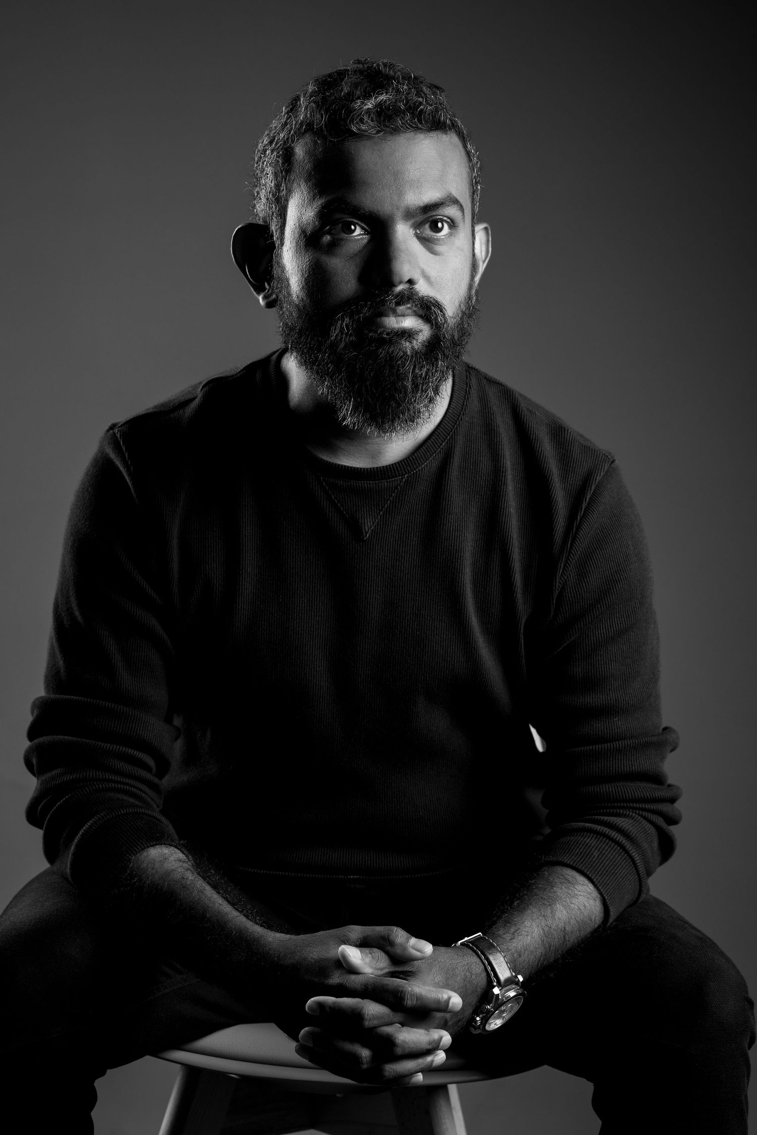 Black and white portrait of a person in a black sweater with a beard against dark background.
