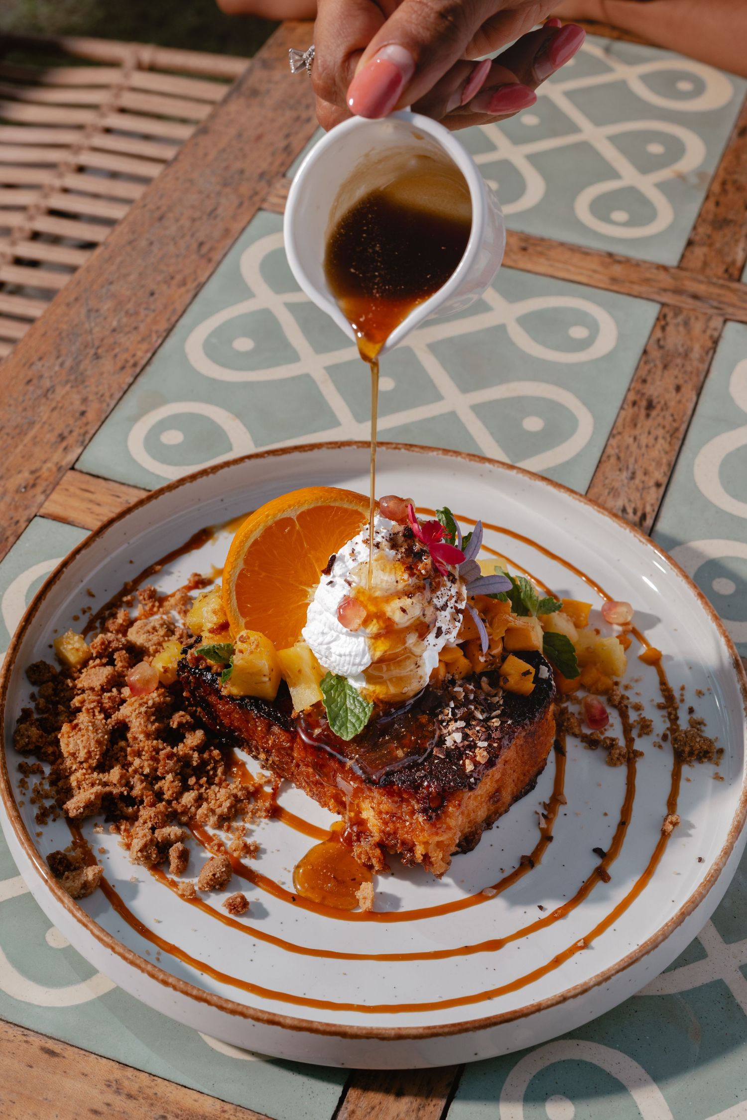 A decadent dessert plate with whipped cream, orange slice and caramel sauce being drizzled over the top.