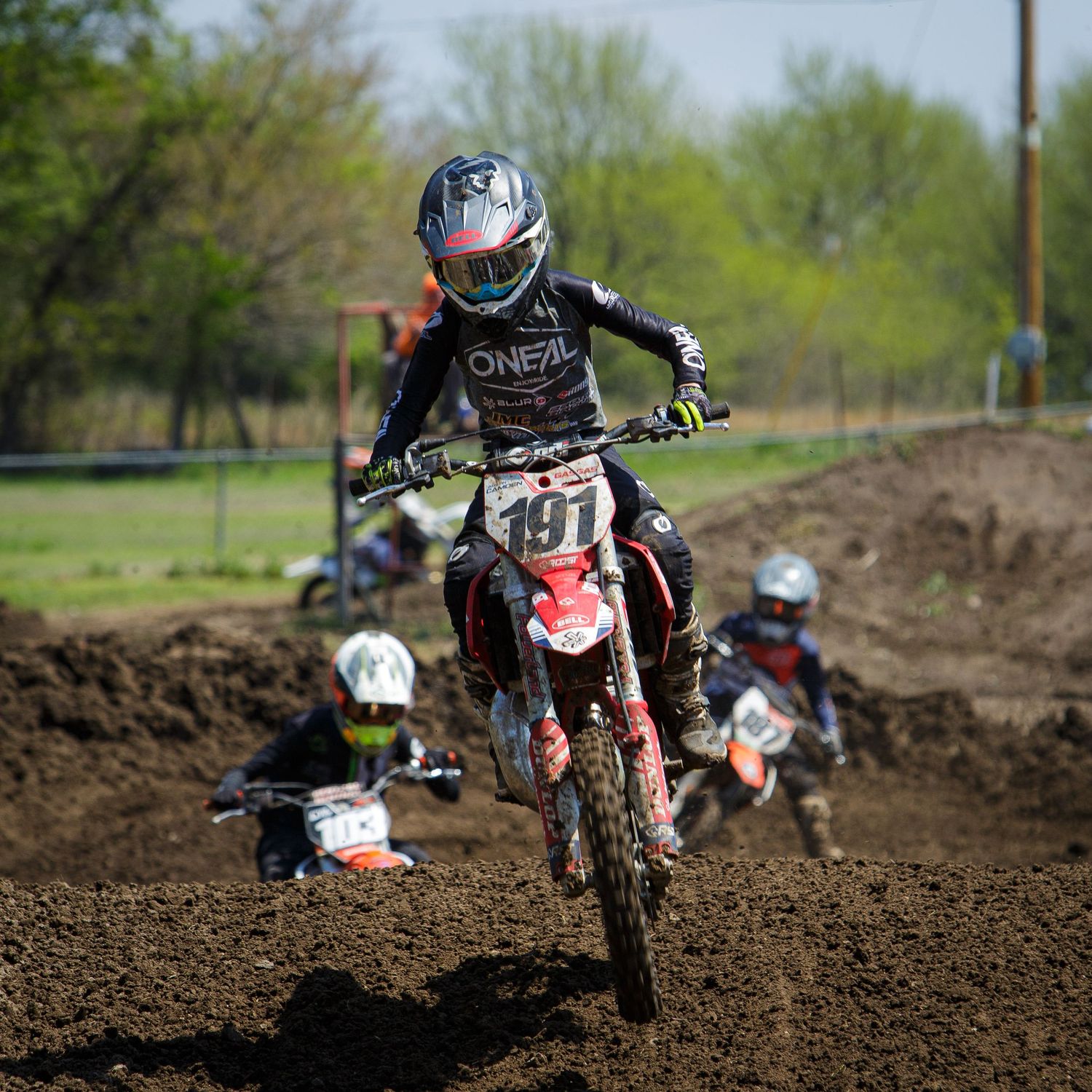 Dirt bike rider getting airborne on muddy motocross track during competition.