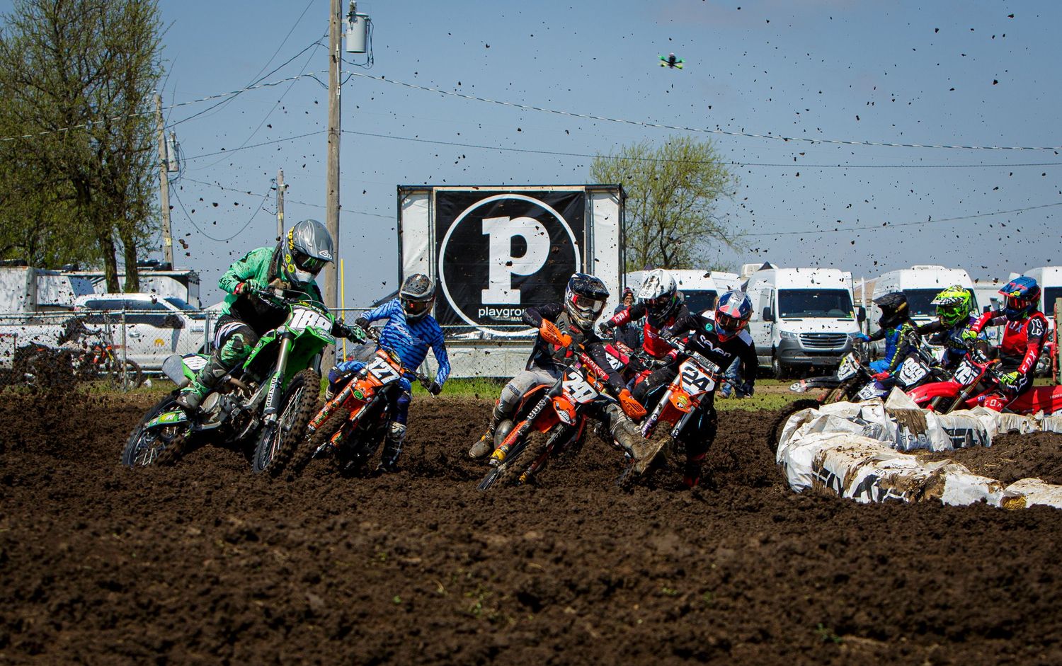 Group of motocross riders race through muddy corner during competitive event.