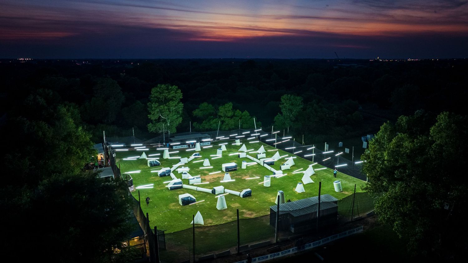 Illuminated RV camping spots arranged in a geometric pattern at dusk with trees in the background.