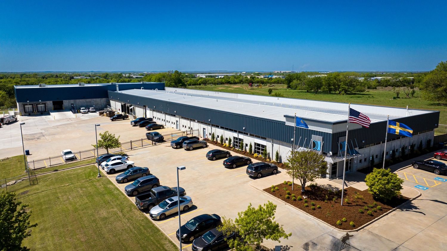 Modern commercial warehouse building with parked cars and landscaping from aerial view.