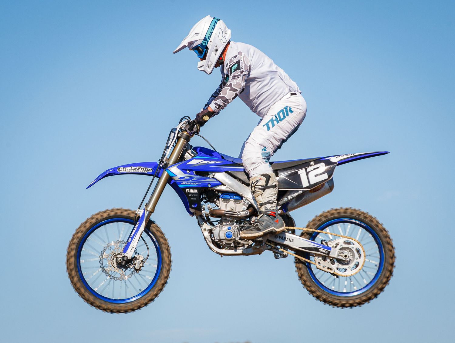Motocross rider performs jump on blue dirt bike against clear sky background.
