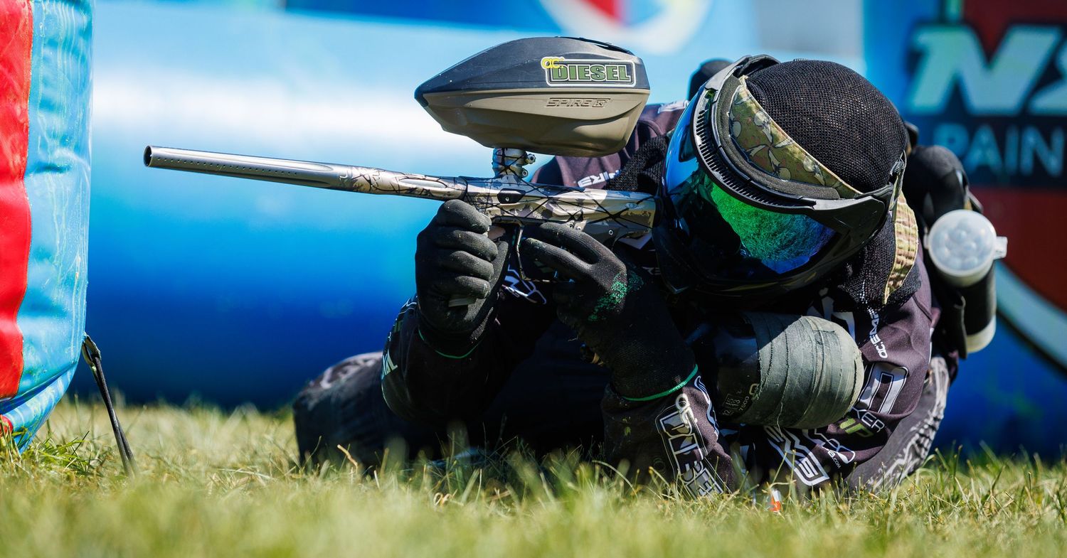 Player taking defensive position with paintball marker behind inflatable bunker.