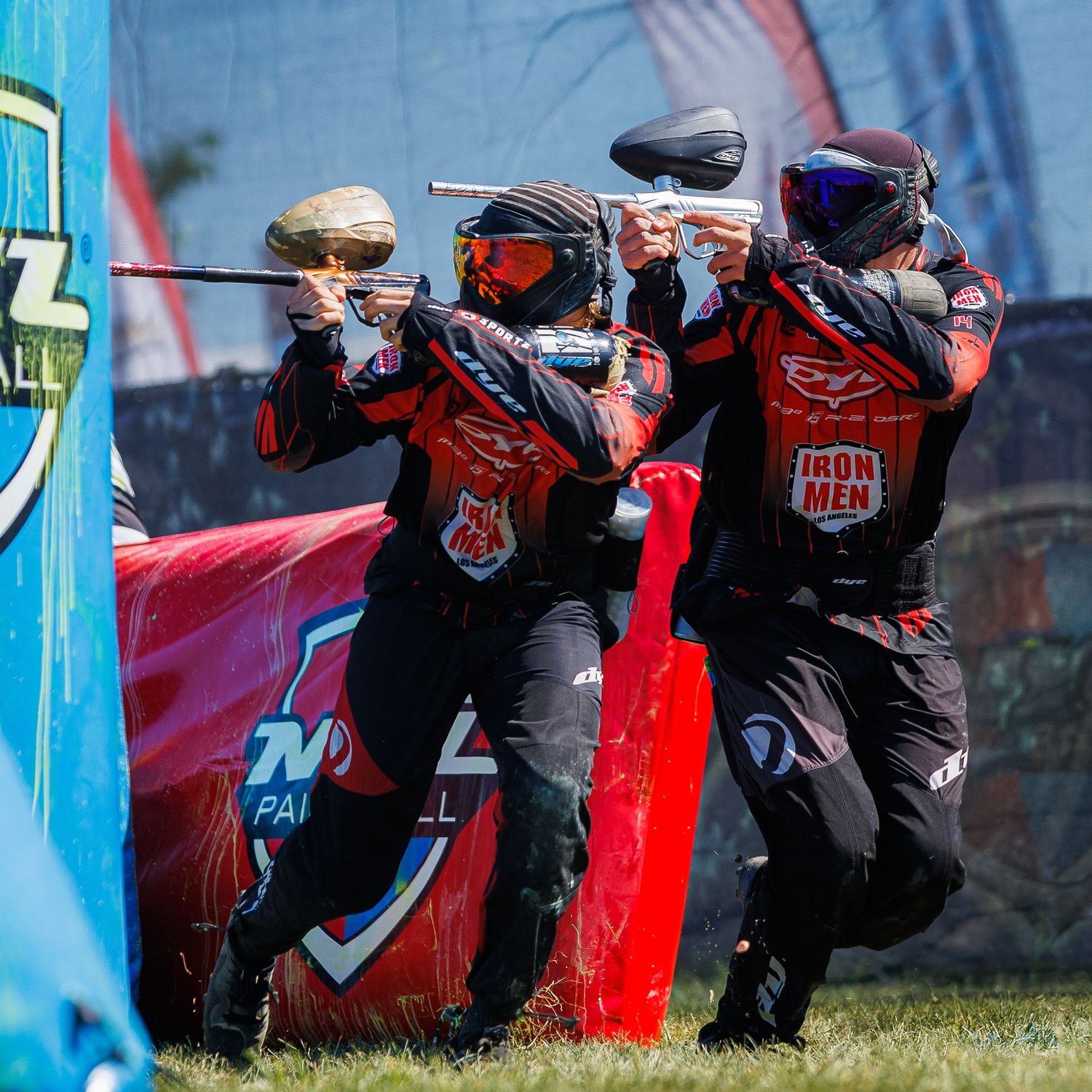 Team of paintball players in red jerseys moving tactically during tournament match.