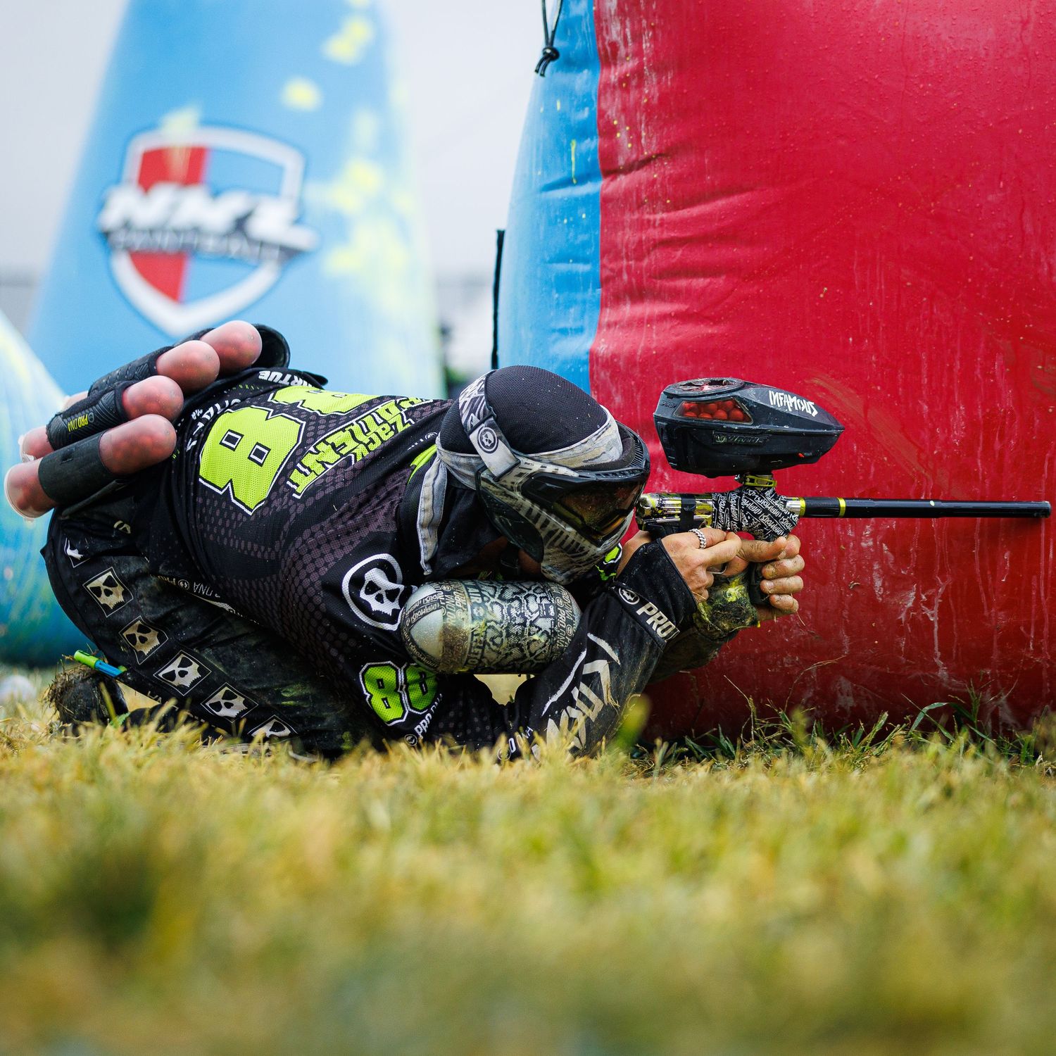 Paintball player in tactical gear lies prone behind inflatable cover during match.