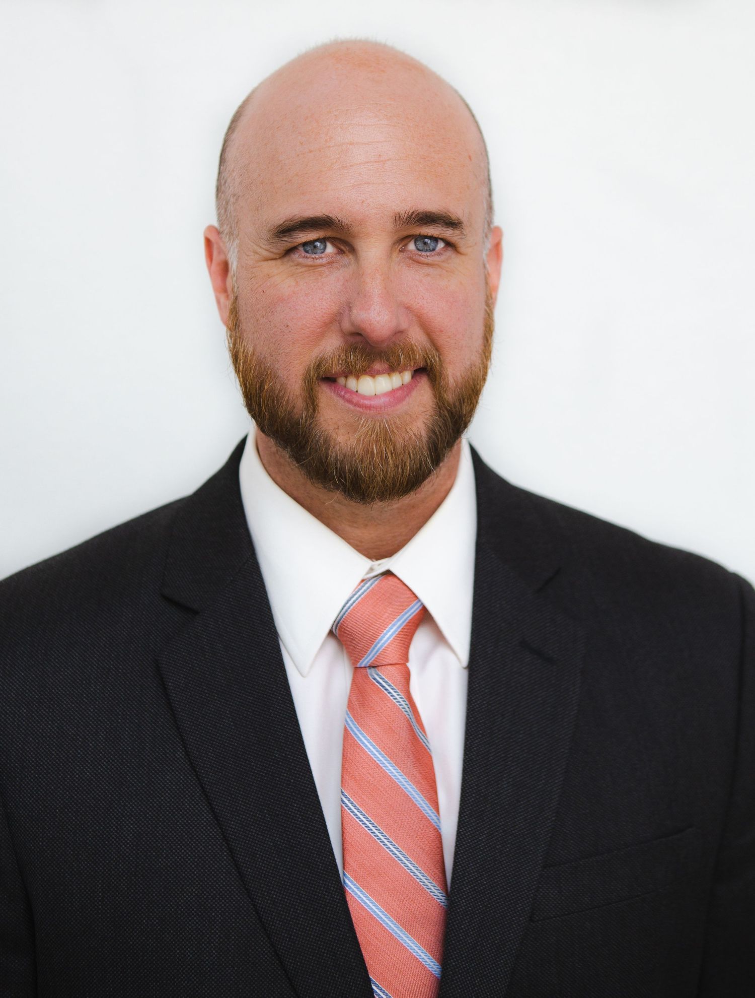 Professional headshot of a person in a dark suit and coral striped tie against a white background.