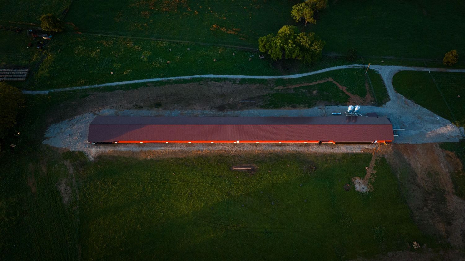 Aerial view of a long red barn structure with curved driveway at dusk.