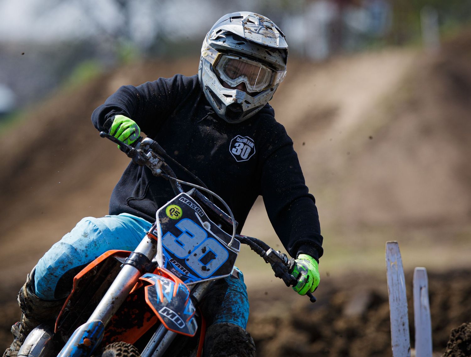 Motocross rider in protective gear races through muddy track corner.