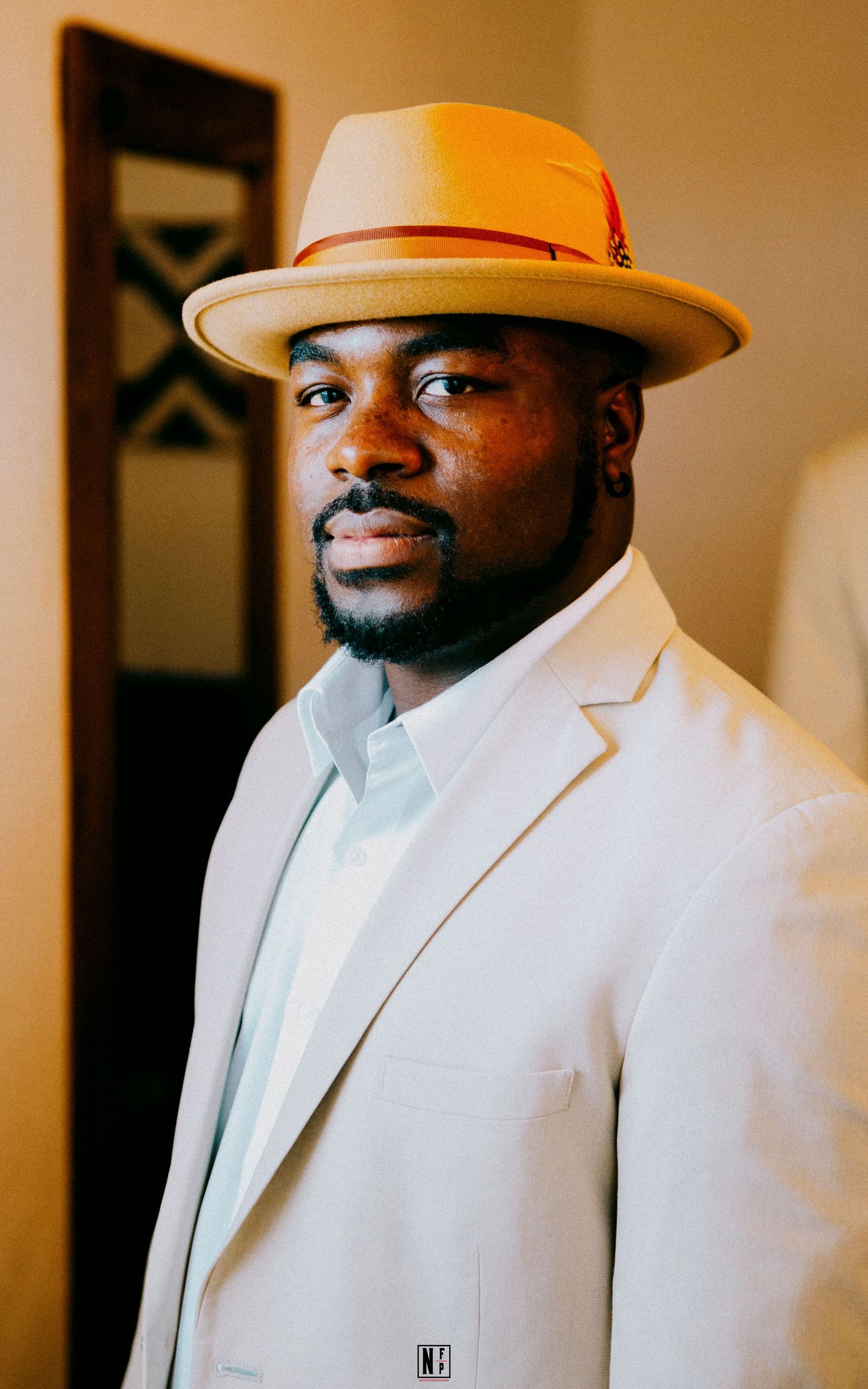 Stylish portrait of person in white suit jacket and cream fedora with orange band.