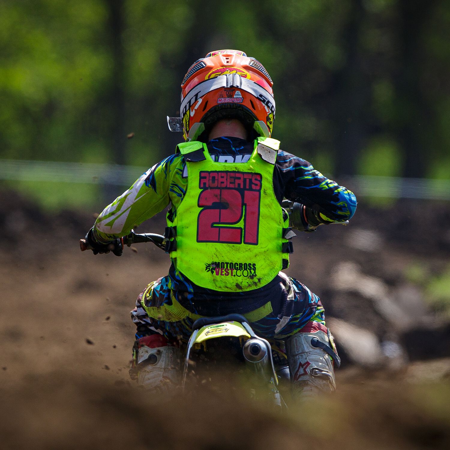 Motocross rider in bright green jersey kicks up dirt while racing on outdoor track.