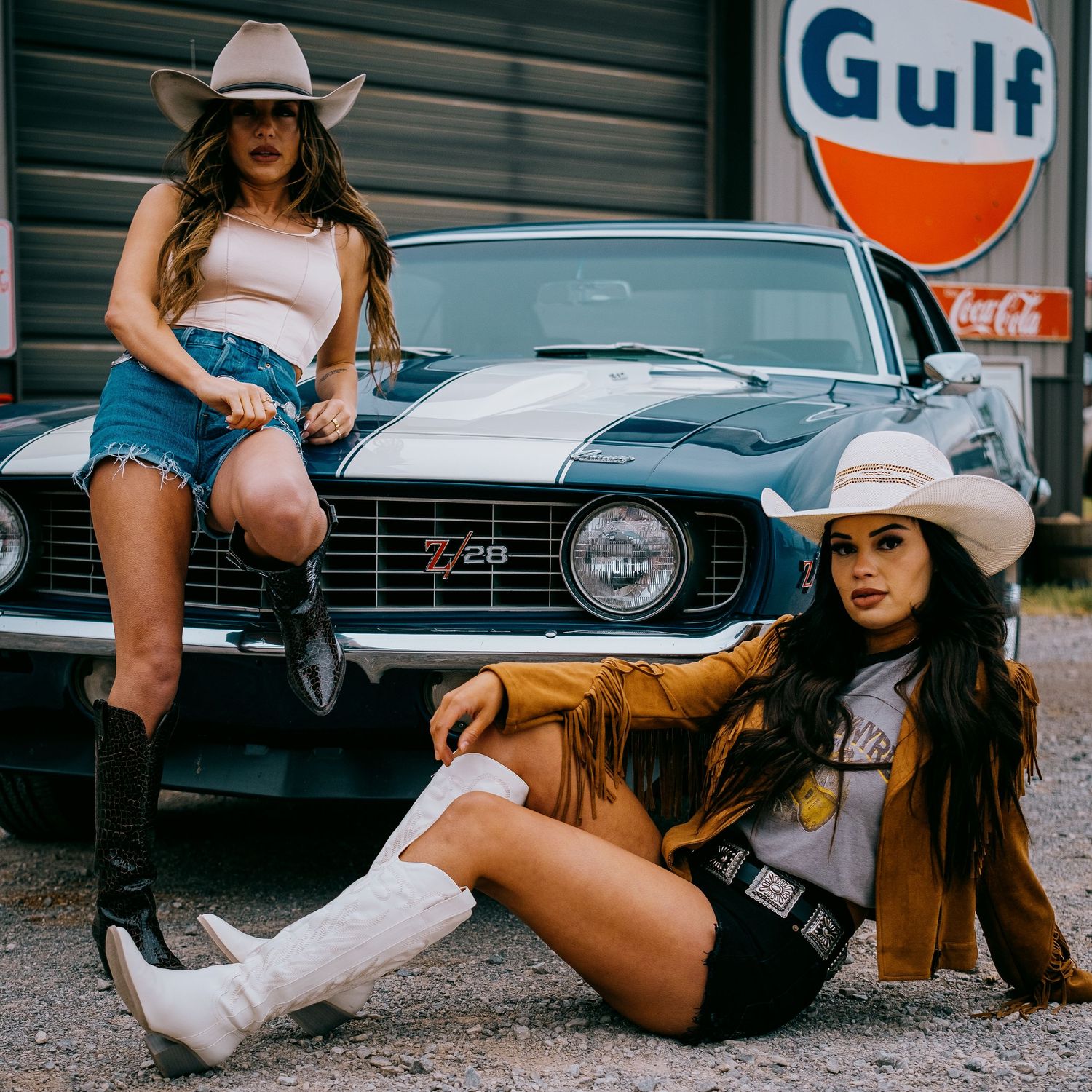 Two women in western wear pose with vintage Camaro at Gulf gas station.