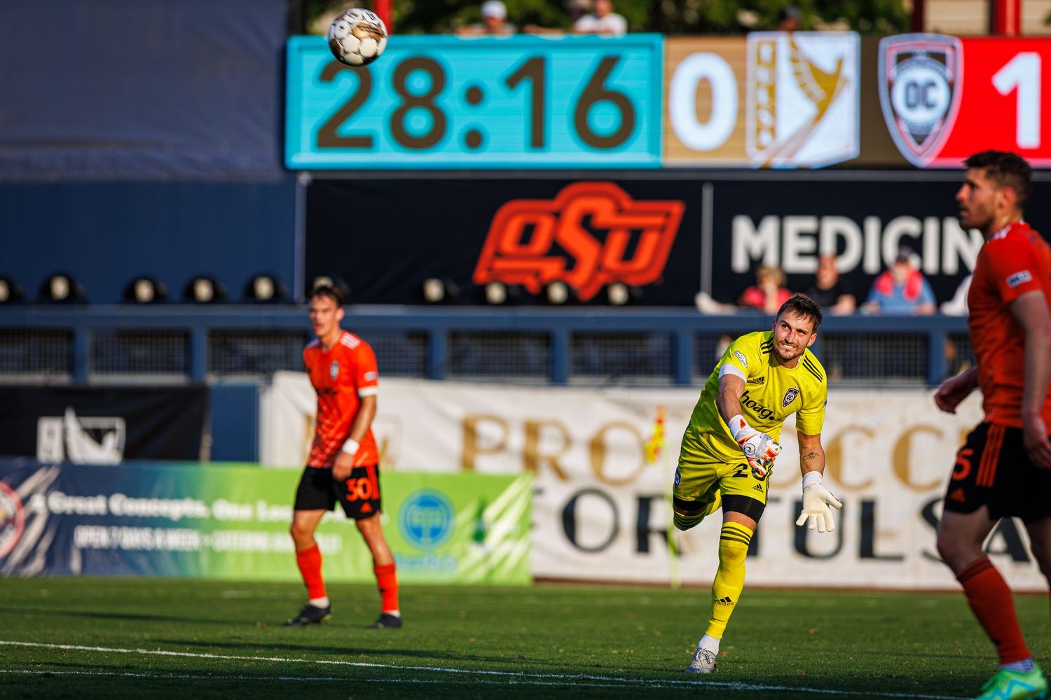 Soccer players in orange and yellow jerseys compete for the ball during an intense match on a grass field.