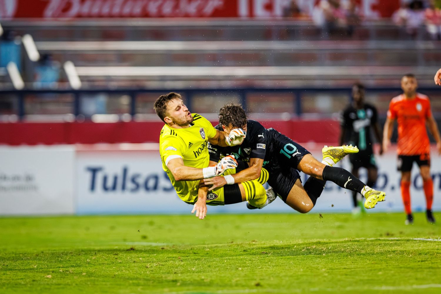 A soccer goalkeeper makes a dramatic diving save during a match, stretching horizontally through the air.