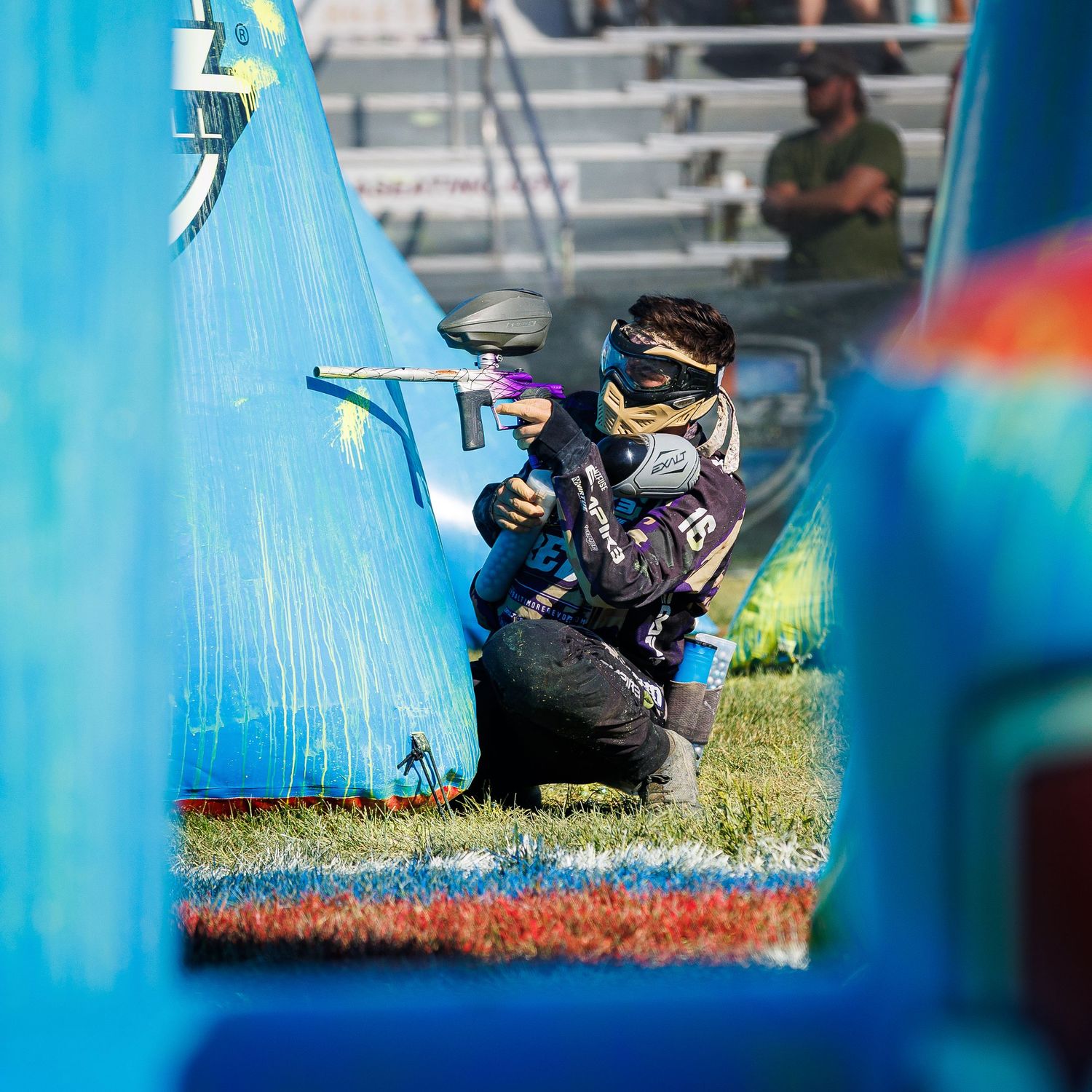 Paintball competitor aims through inflatable bunker during tournament match.