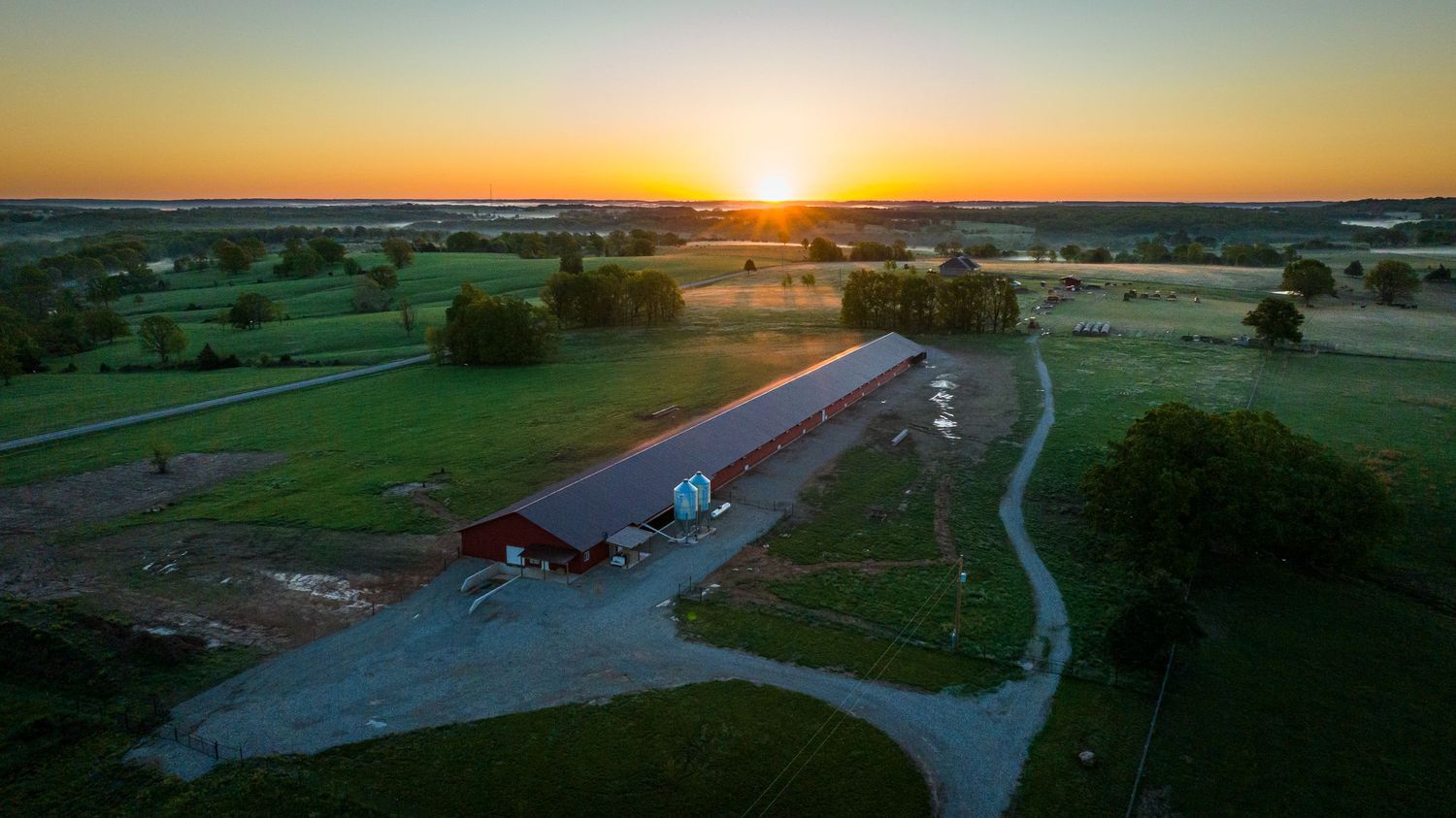 Aerial view of a rural property with winding road during sunset.